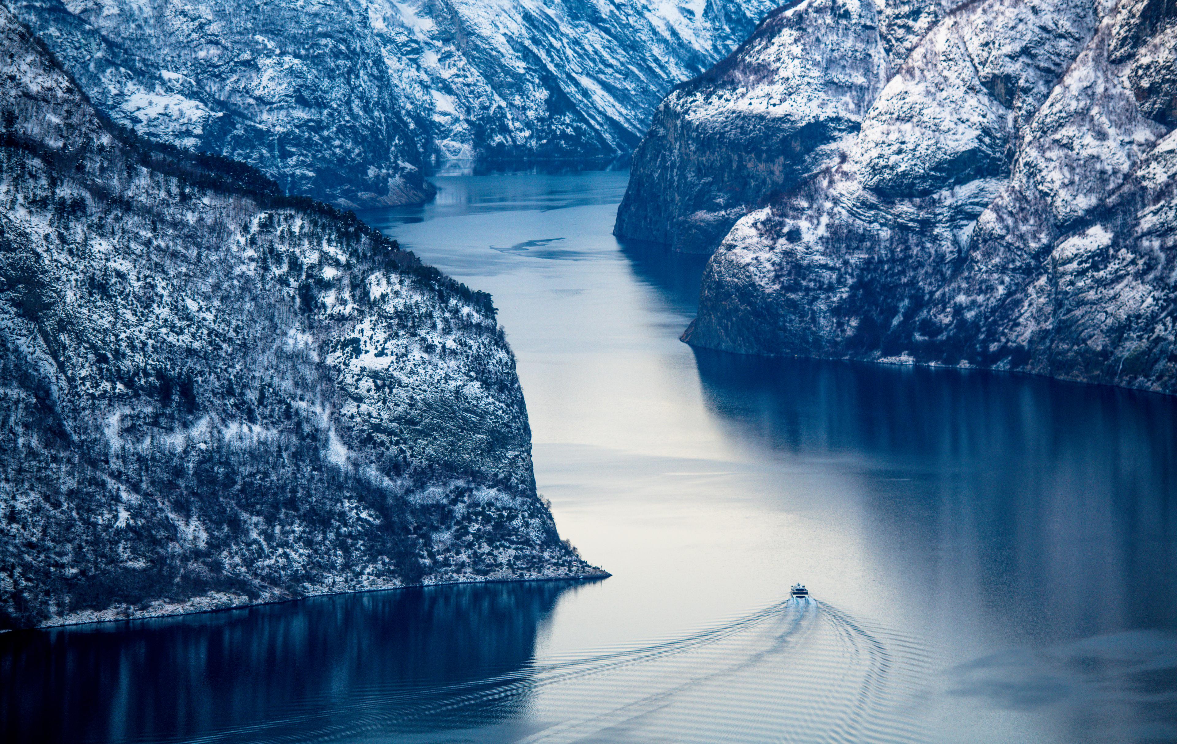 A ferry sails on the fjord in winter, seen from a bird's eye perspective.