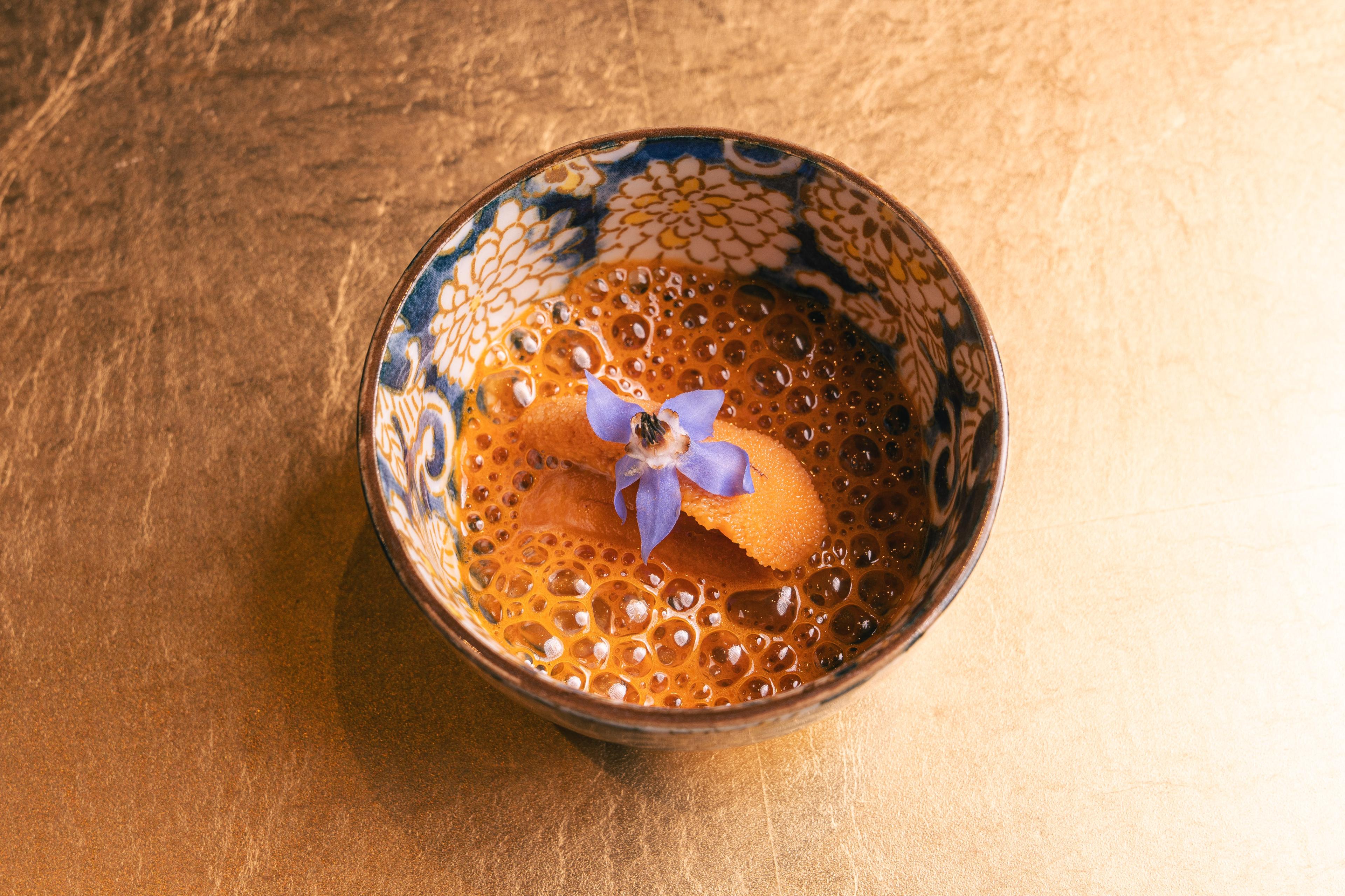 A patterned bowl with a whipped, airy orange cream, topped with a purple flower.