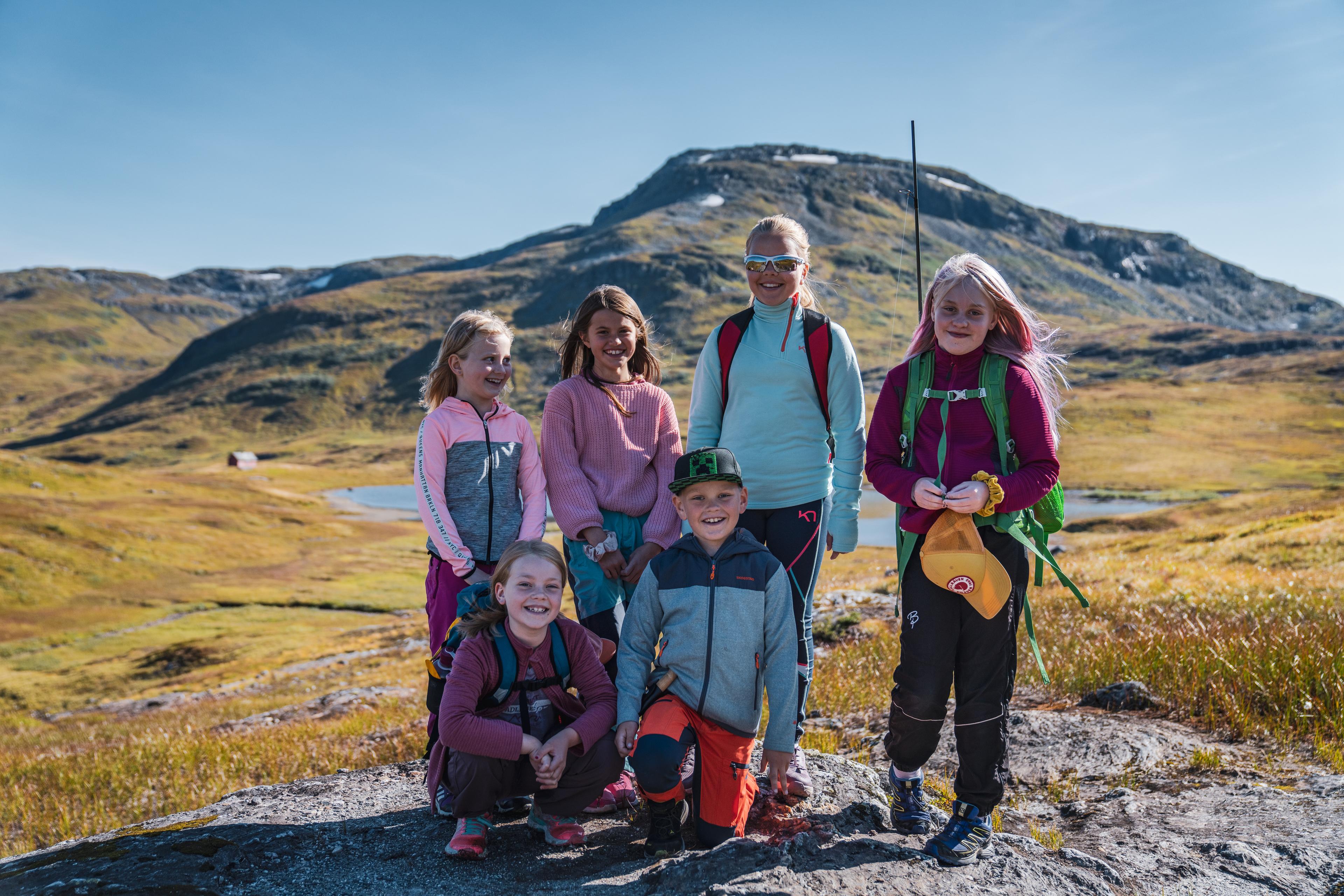 En gruppe smilende barn poserer for fotografen foran et fjellvann.