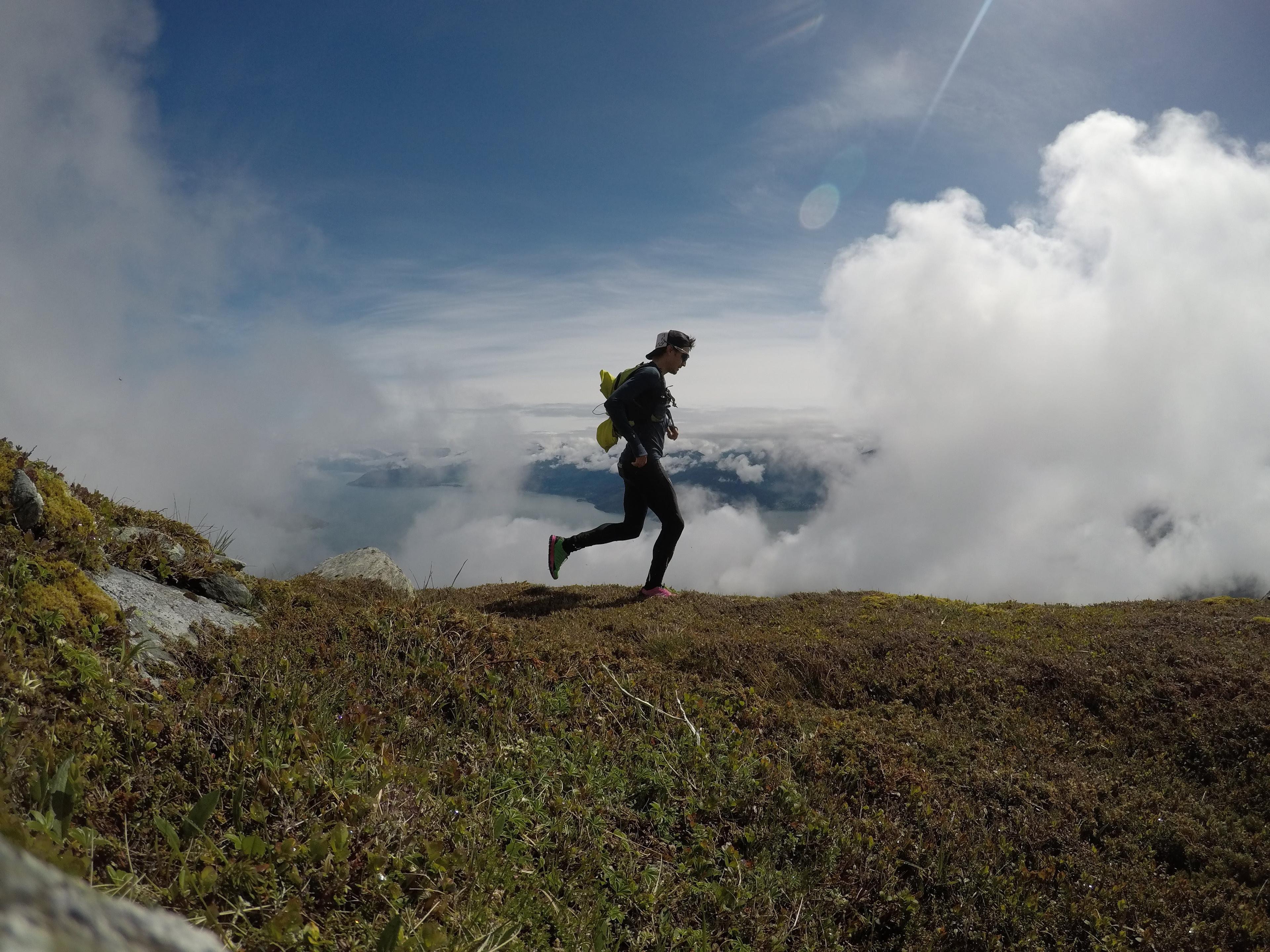 Mann på joggetur høyt oppe på fjellet, med utsikt over fjord og snødekte fjell.