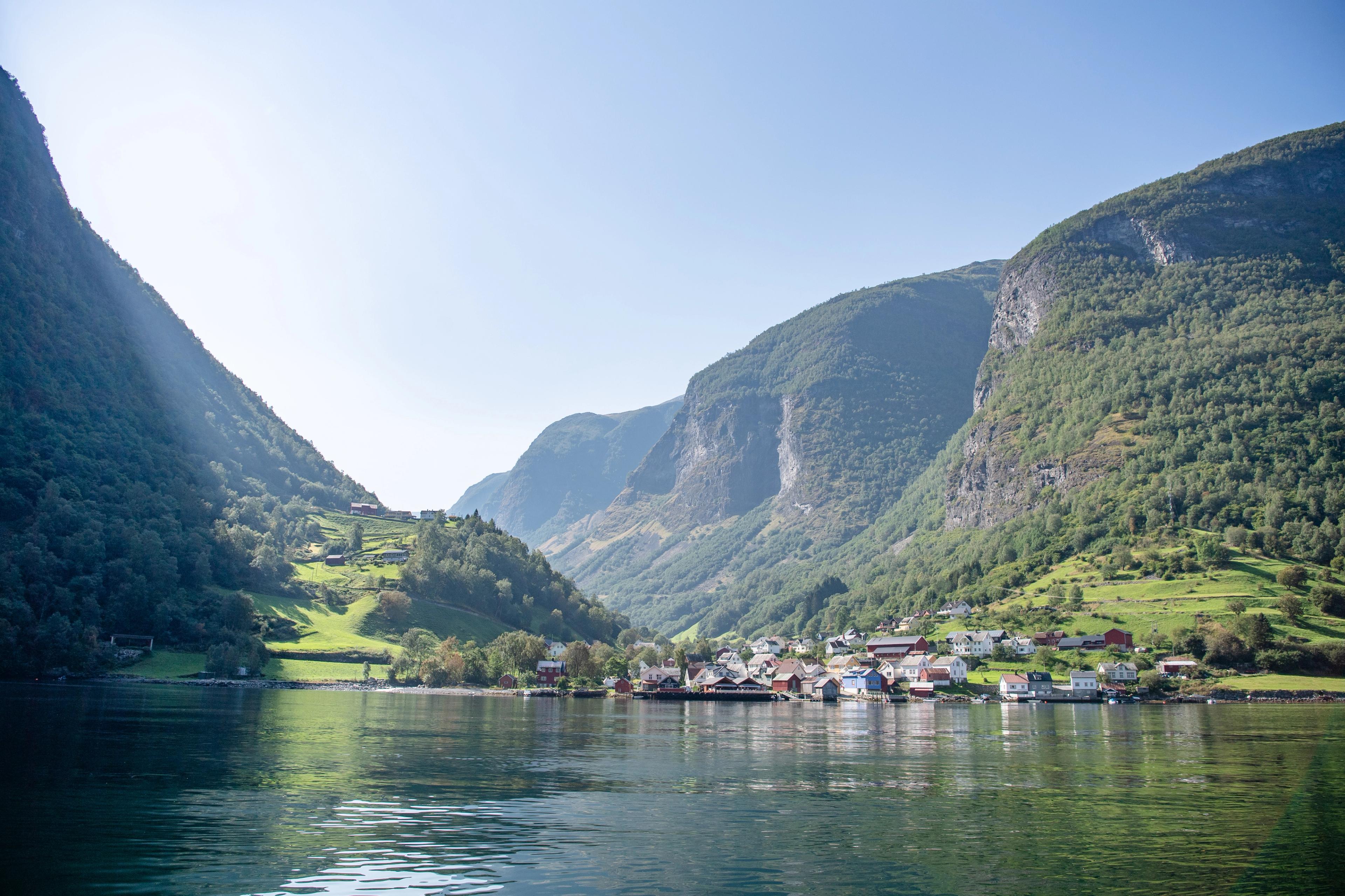 Das Dorf Undredal, an einem sonnigen Sommertag vom Fjord aus gesehen, umgeben von steilen, aufragenden Bergen.