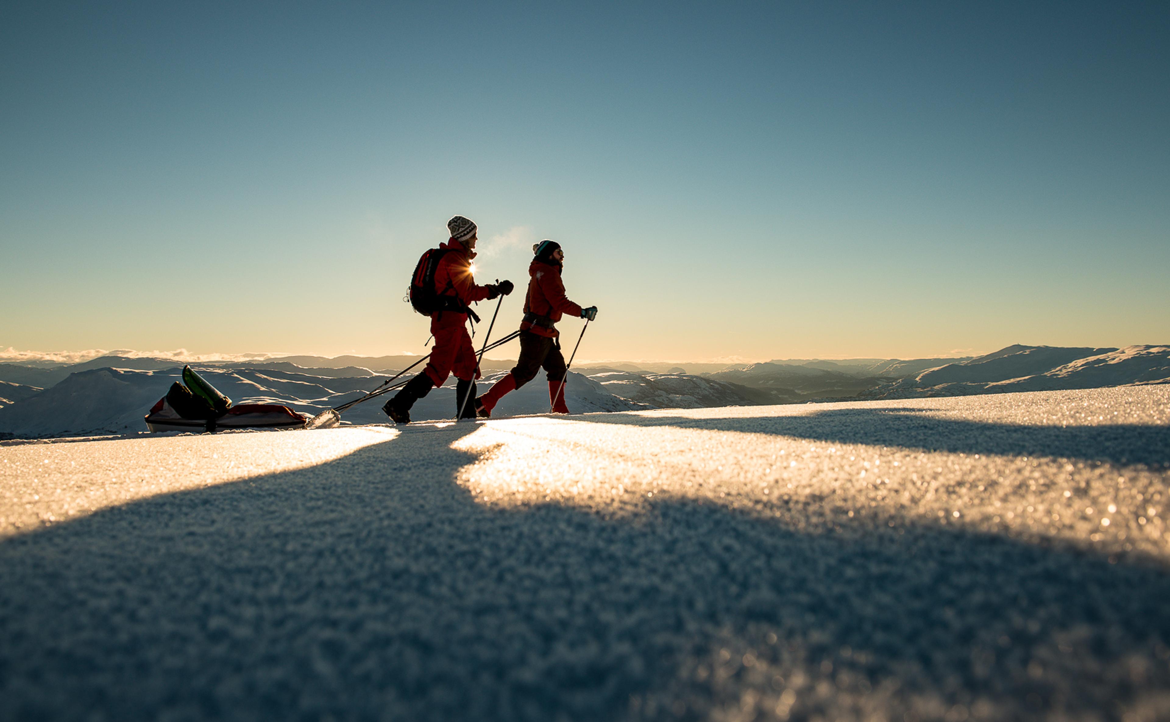 Et par går på ski med pulk over fjellplatået i ettermiddagssol.
