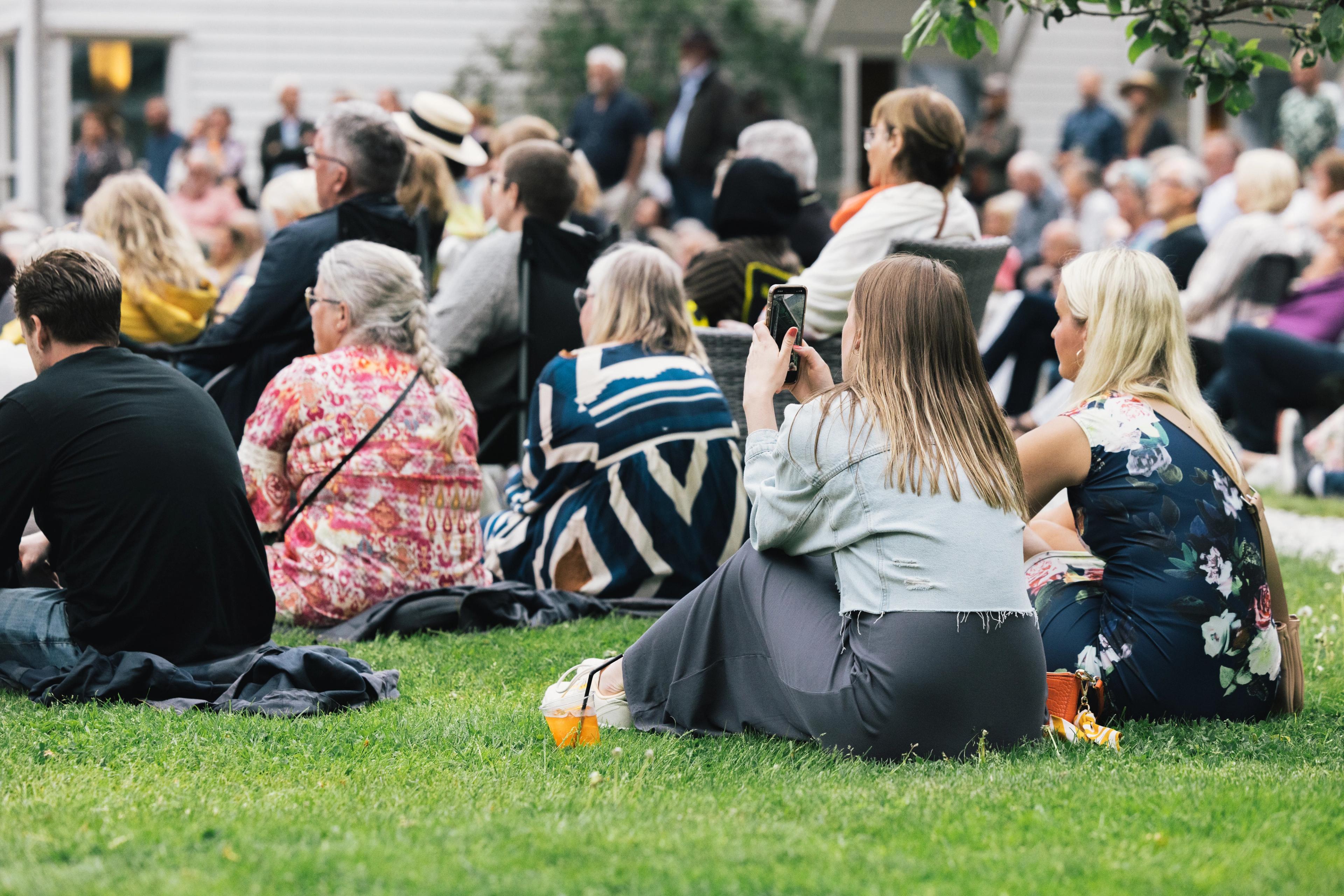Sommerkledde gjester sitter med ryggen til på Hagekonsert på Fretheim Hotel