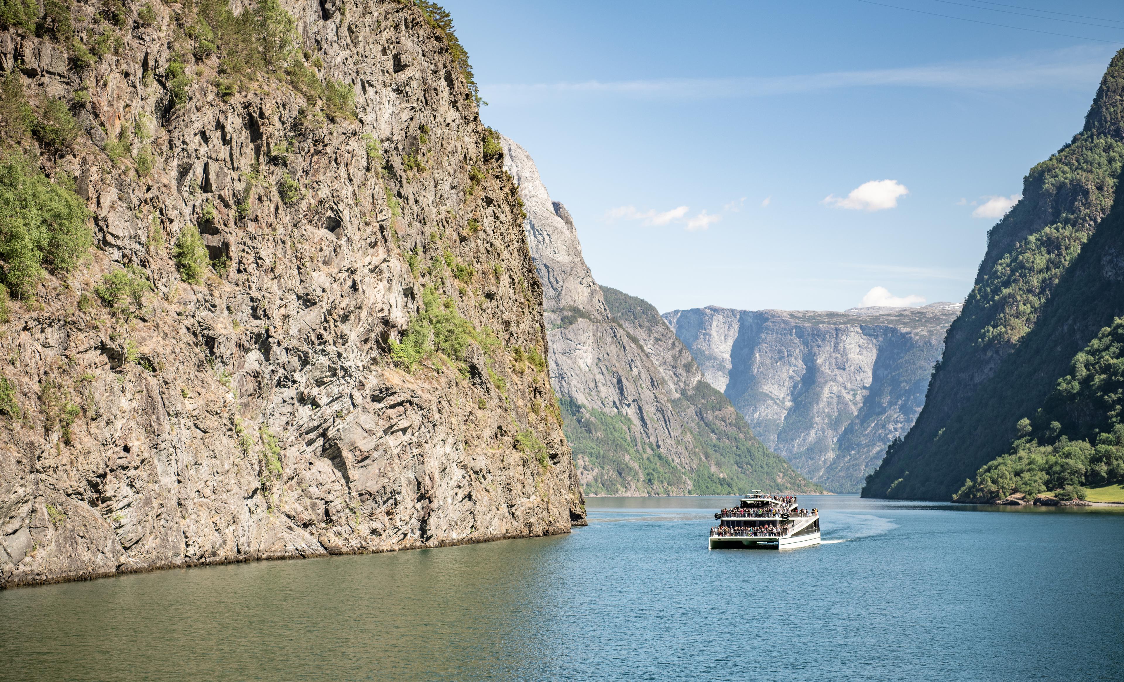 Fjordcruise med passasjerar på veg til Flåm om sommaren passerer bratte fjell.