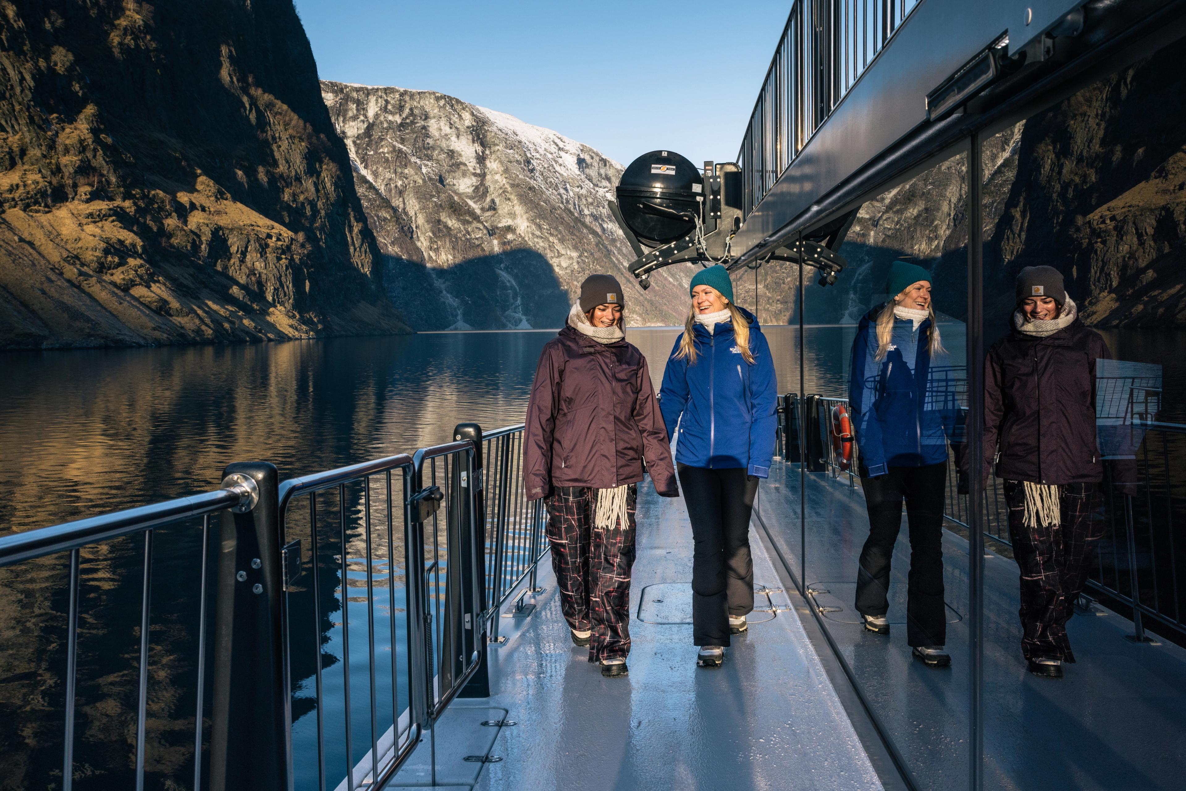 To personer går på dekk på en moderne båt i Nærøyfjorden på vinteren.