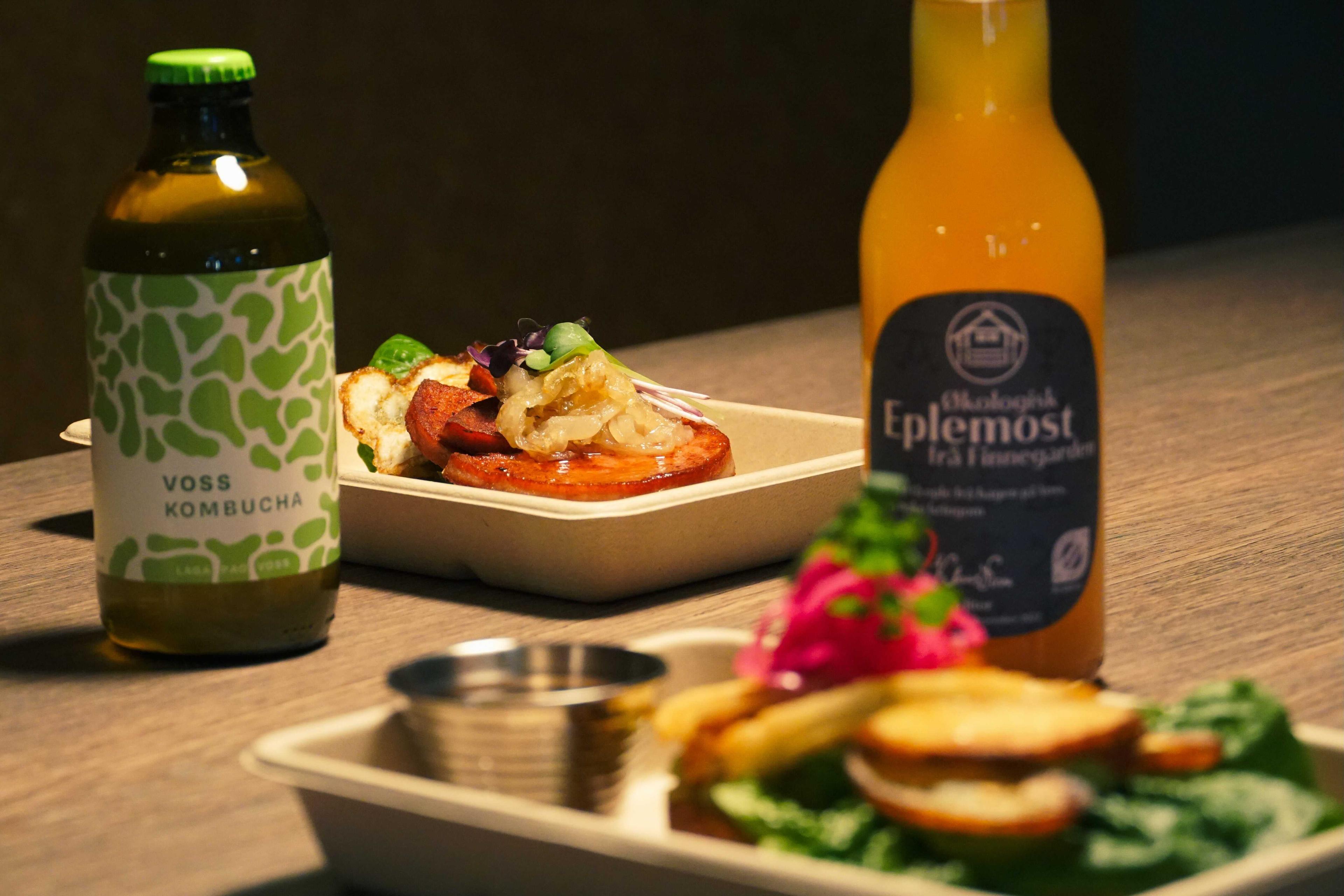 En flaske eplemost, en flaske Voss Kombucha og salat på et bord