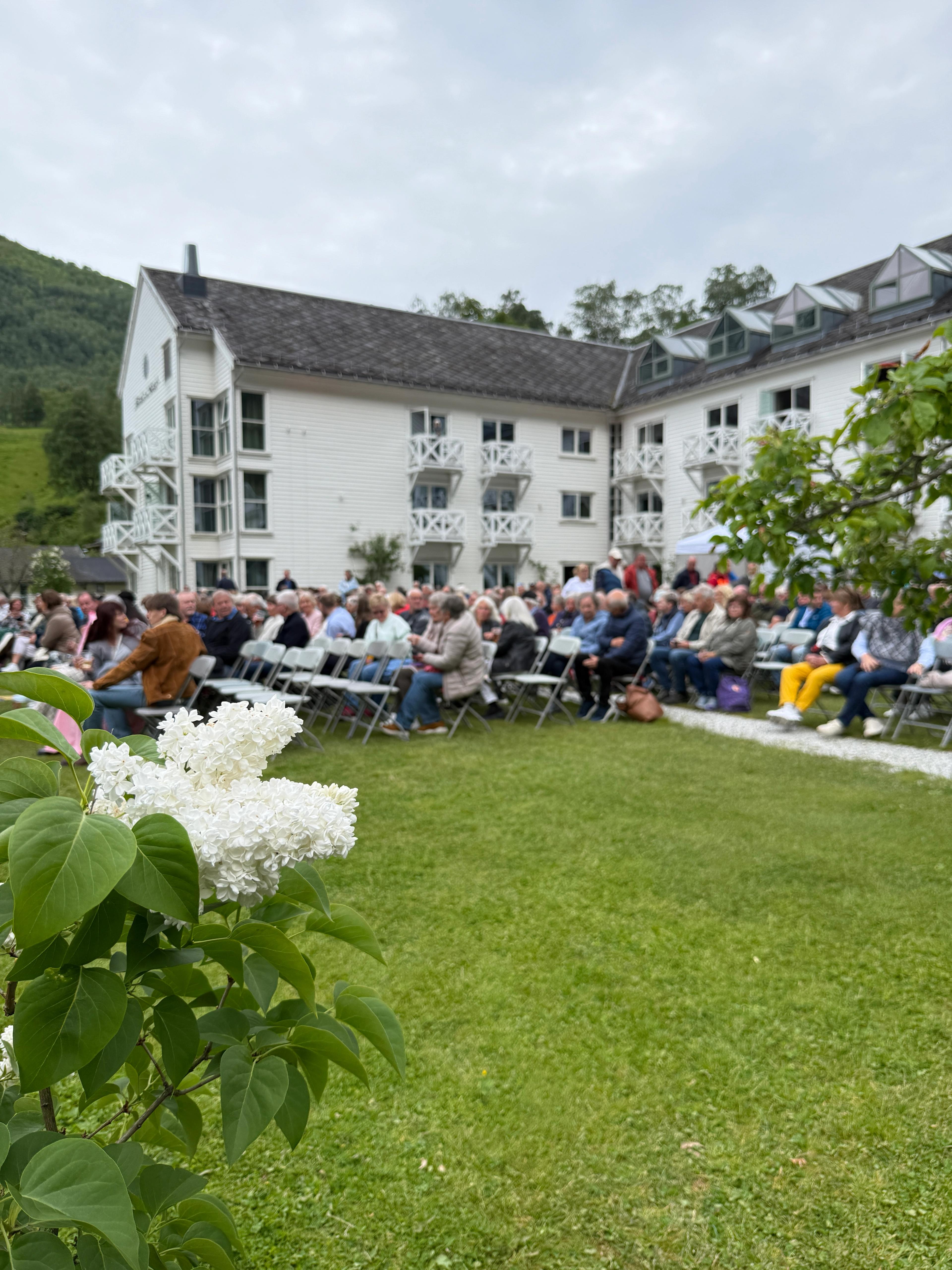 Stemningsbilde fra hagekonsert på Fretheim Hotel. Publikum sitter på stoler i hagen.