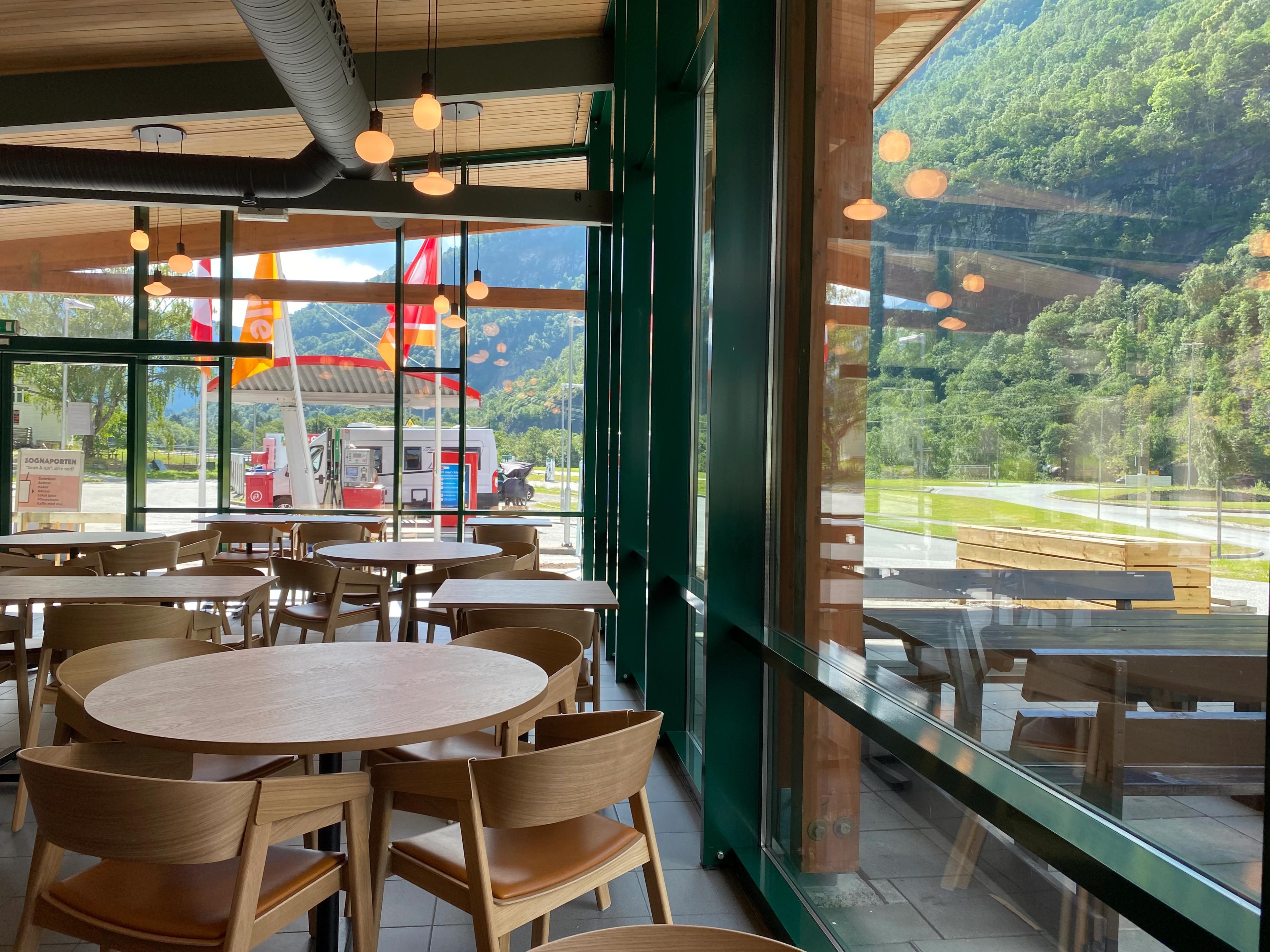 Blick aus einem Restaurant. Die Wände sind vollverglast und zeigen die umliegende norwegische Landschaftt. An den Tischen sitzen keine Menschen.