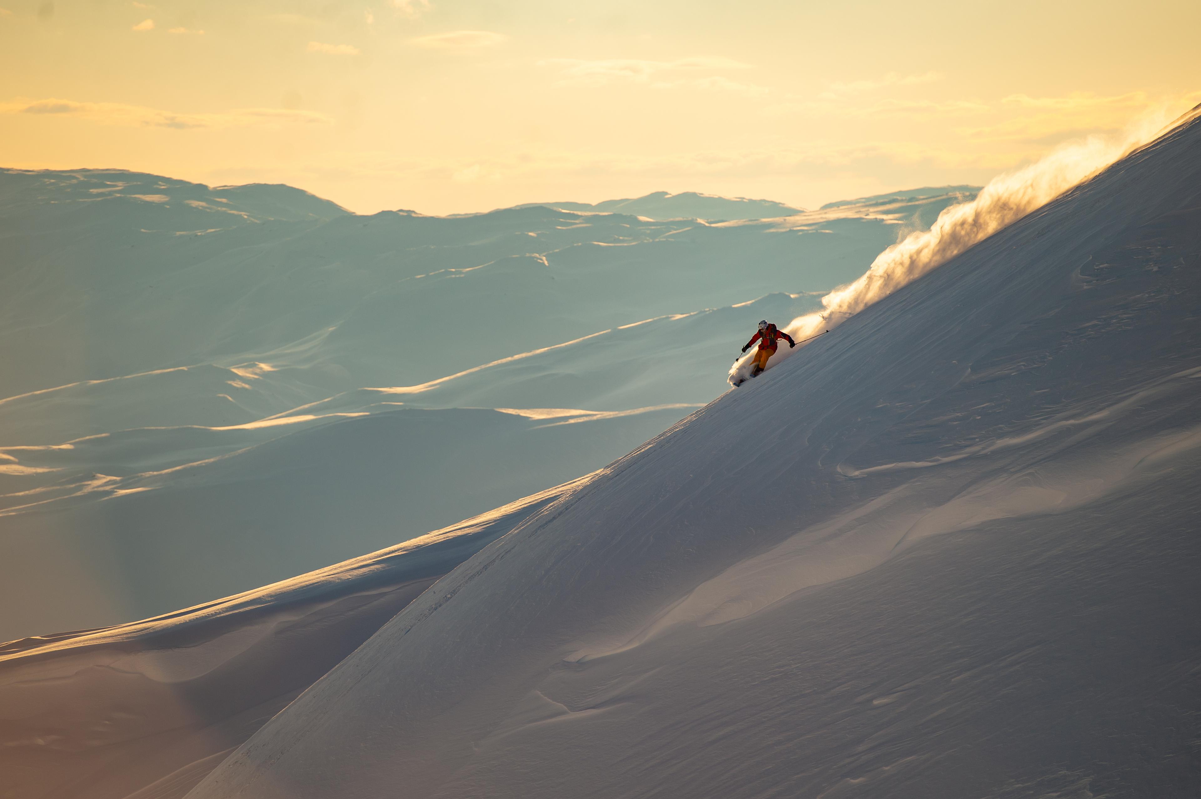 En slalåmkjører står ned bratt bakke idet sola er på vei ned en vinterdag.