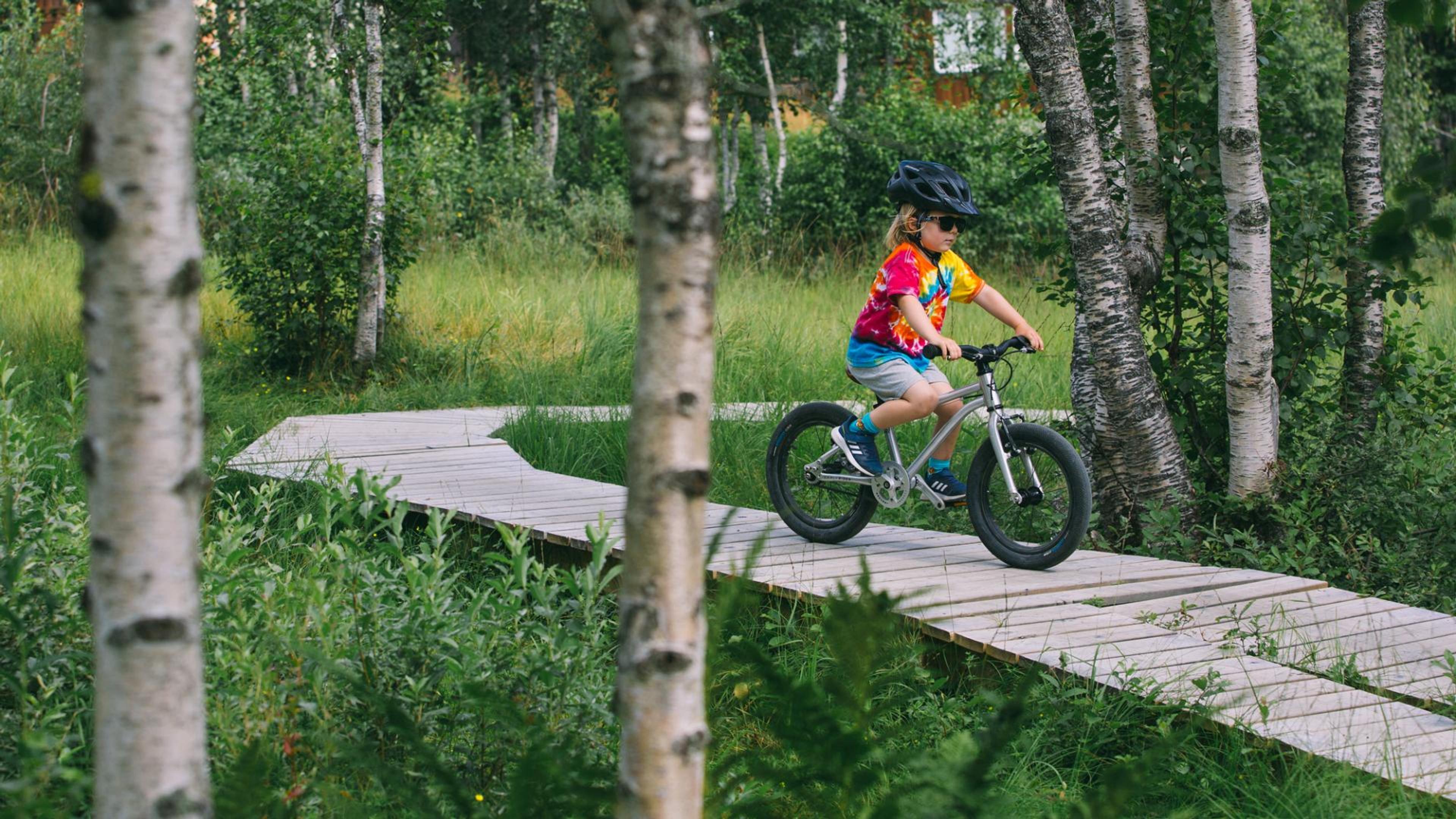 Et barn sykler gjennom terrengløype i skogen.