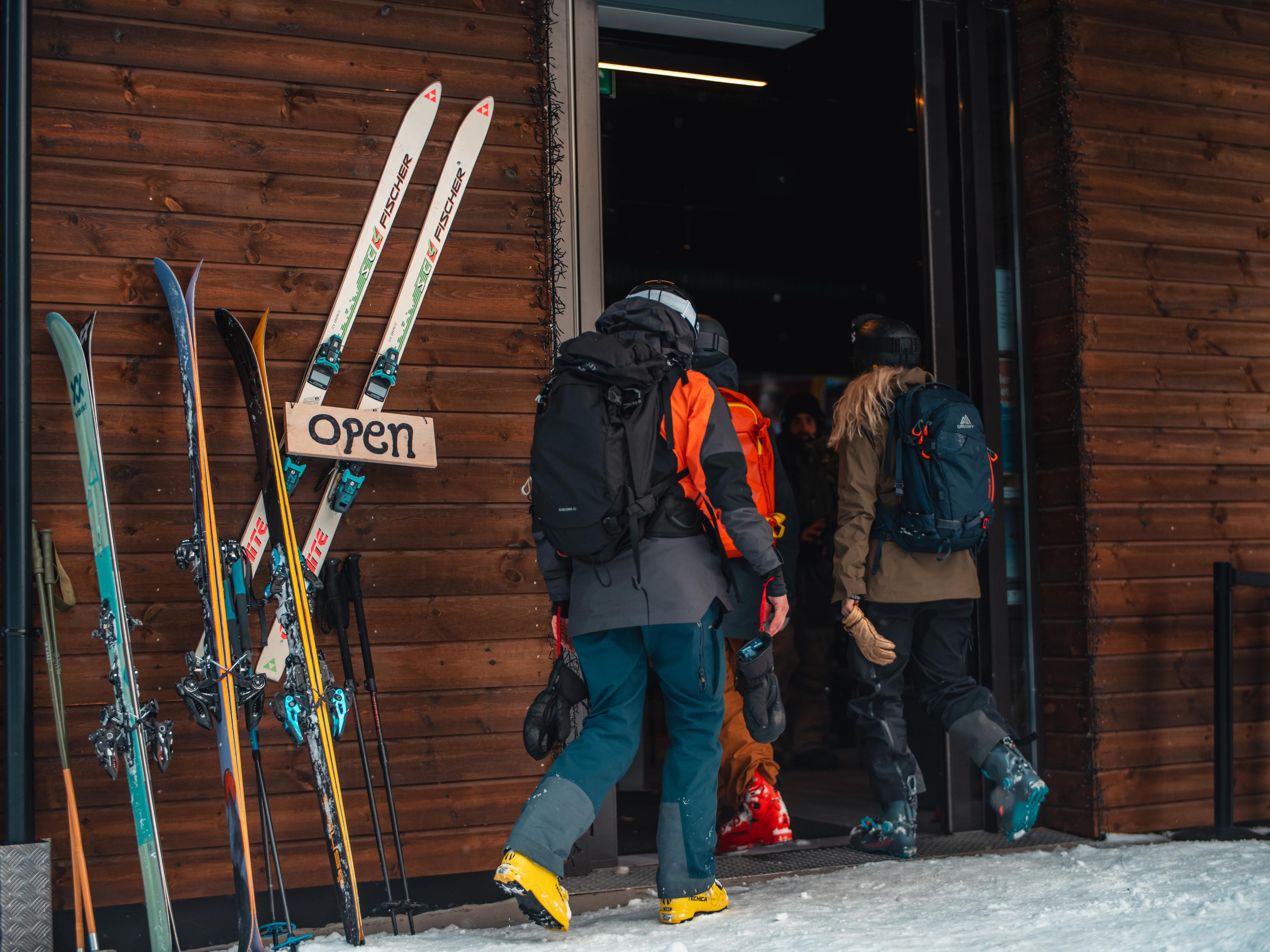 A group of skiers have put down their skis and poles along the wall and enter the cafe to take a break.
