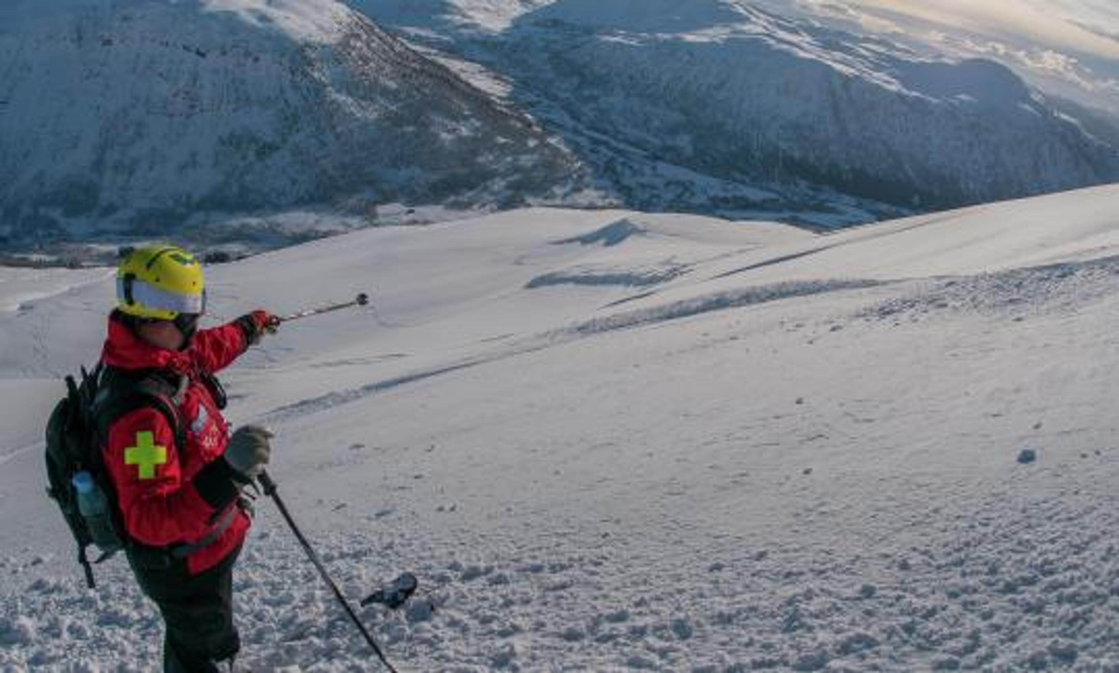 Redningsarbeider peker med staven nedover den snødekte fjellsiden.