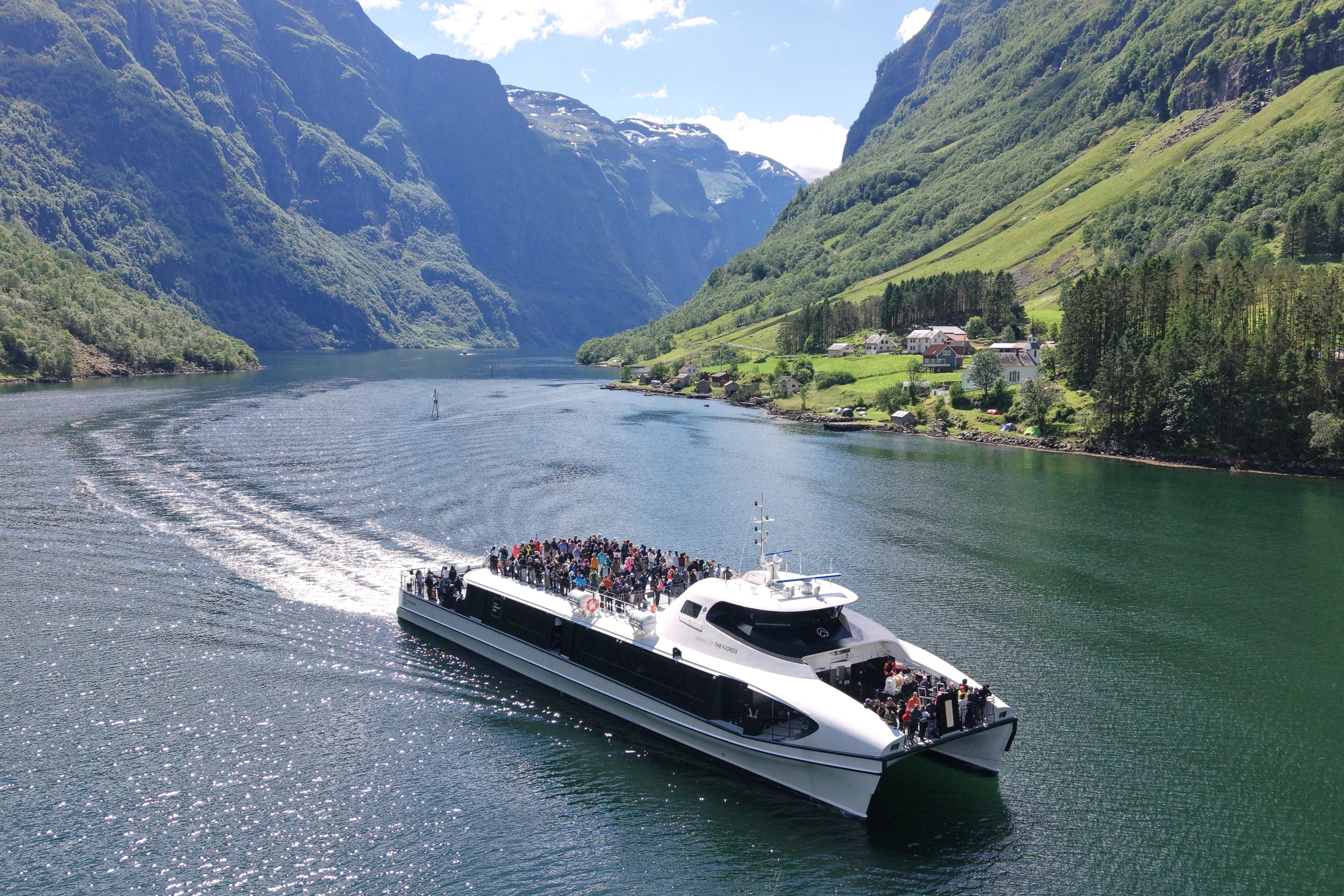 En katamaran kjører gjennom Nærøyfjorden med bratte fjellsider og grønne lier.