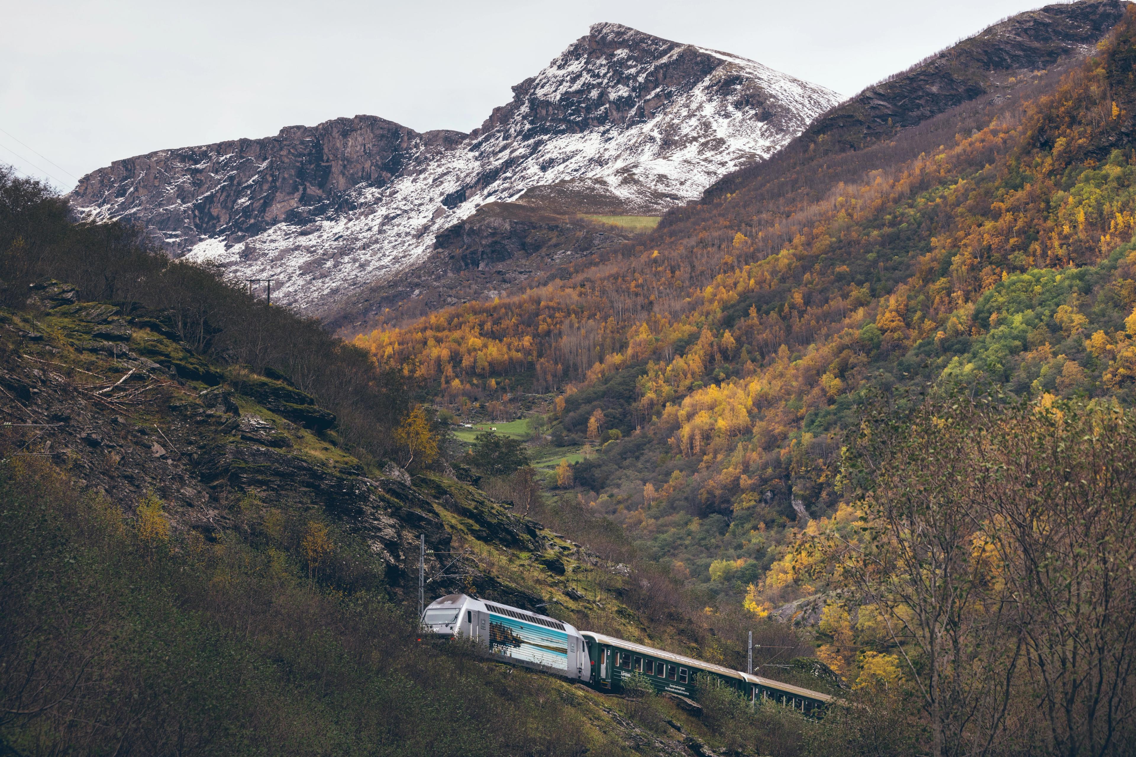  El tren de Flam frente a unas colinas de colores otoñales y una cima con nieve fresca.