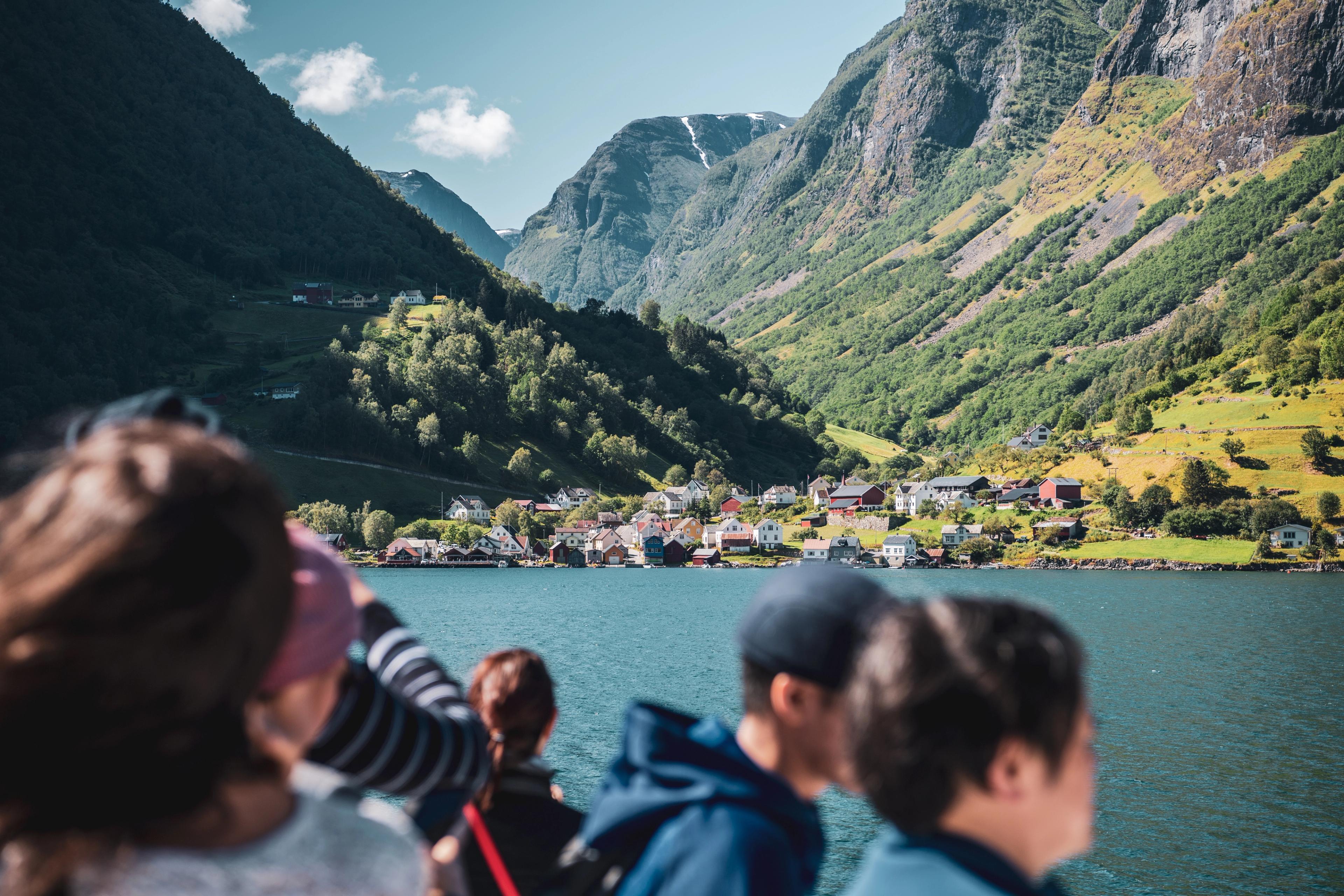 Fjordbygda Undredal sett fra fjorden på en solfylt sommersdag. I forgrunnen uskarpe silhuetter av folk på båten.