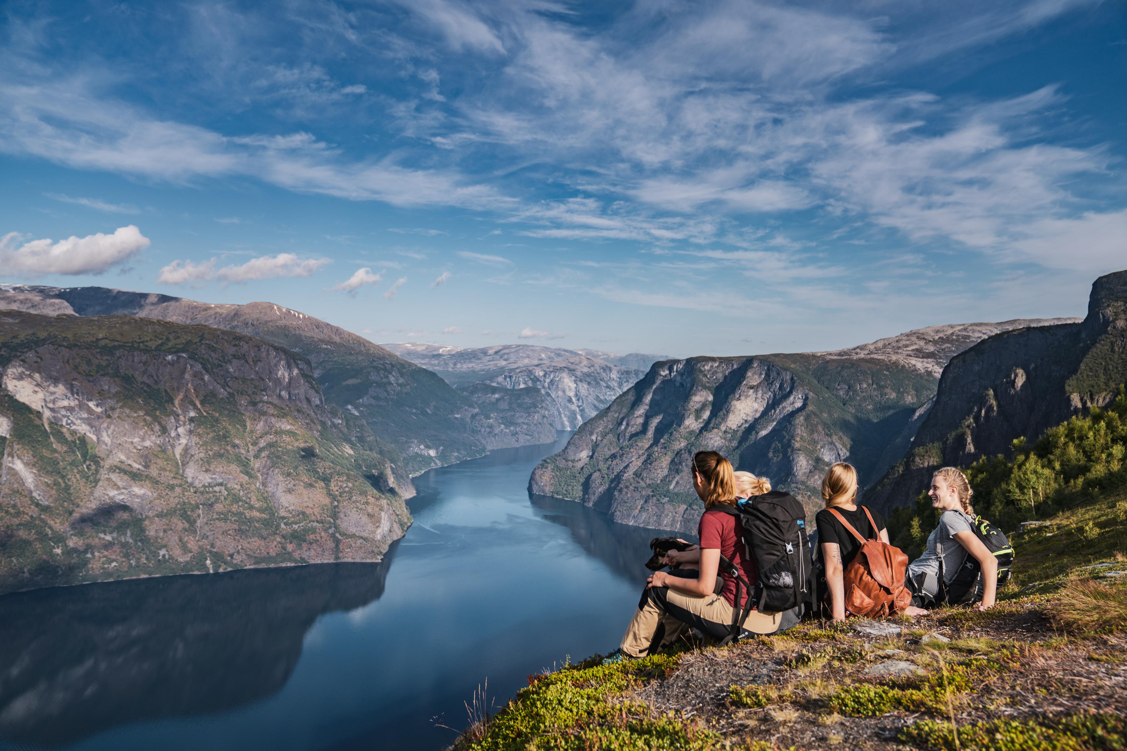 En familie på fjelltur tar en pause på toppen og nyter den mektige utsikten over fjorden og fjellene.