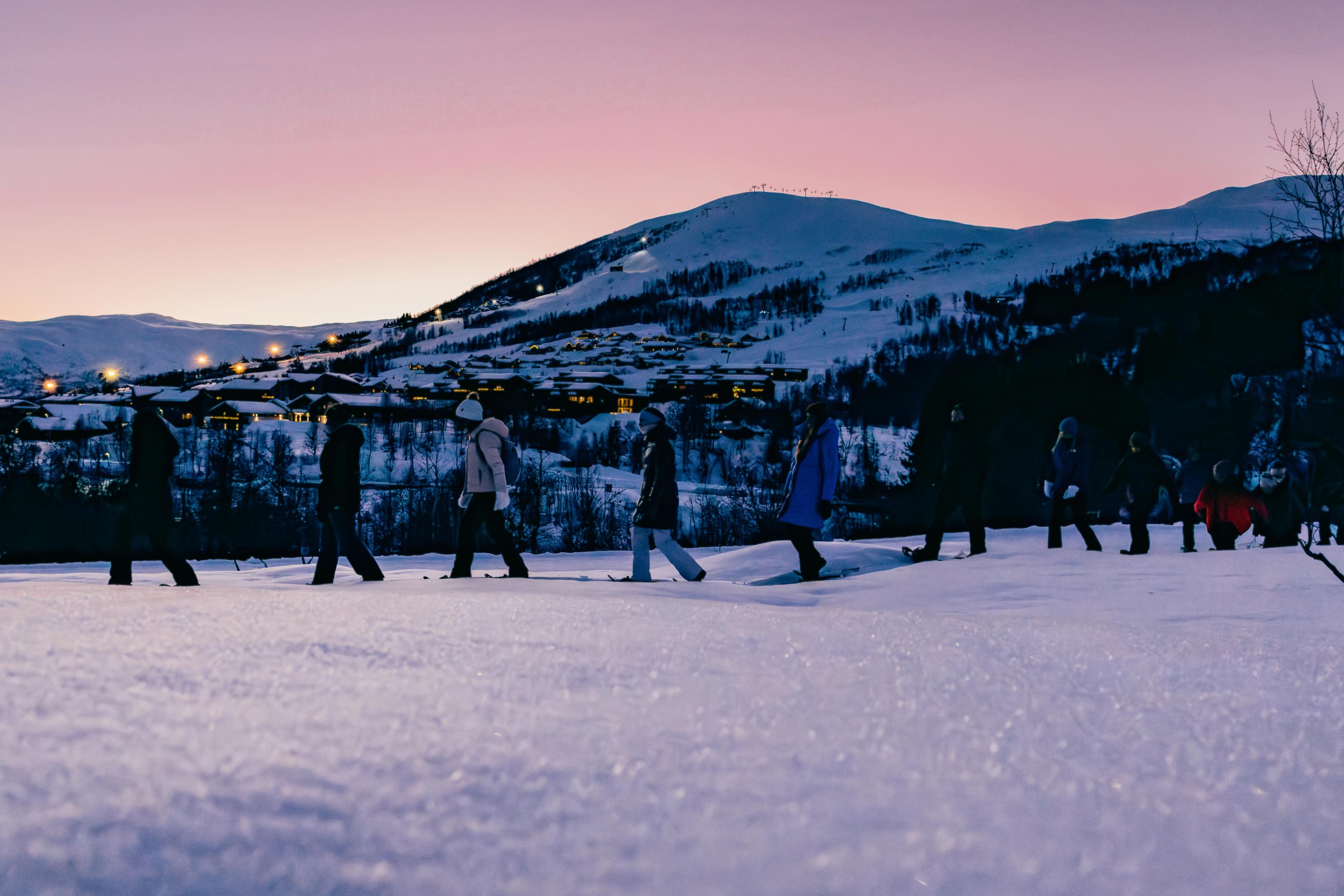 En gjeng som går på truger i skumringtid. Rosa himmel og fjell i bakrgunnen.