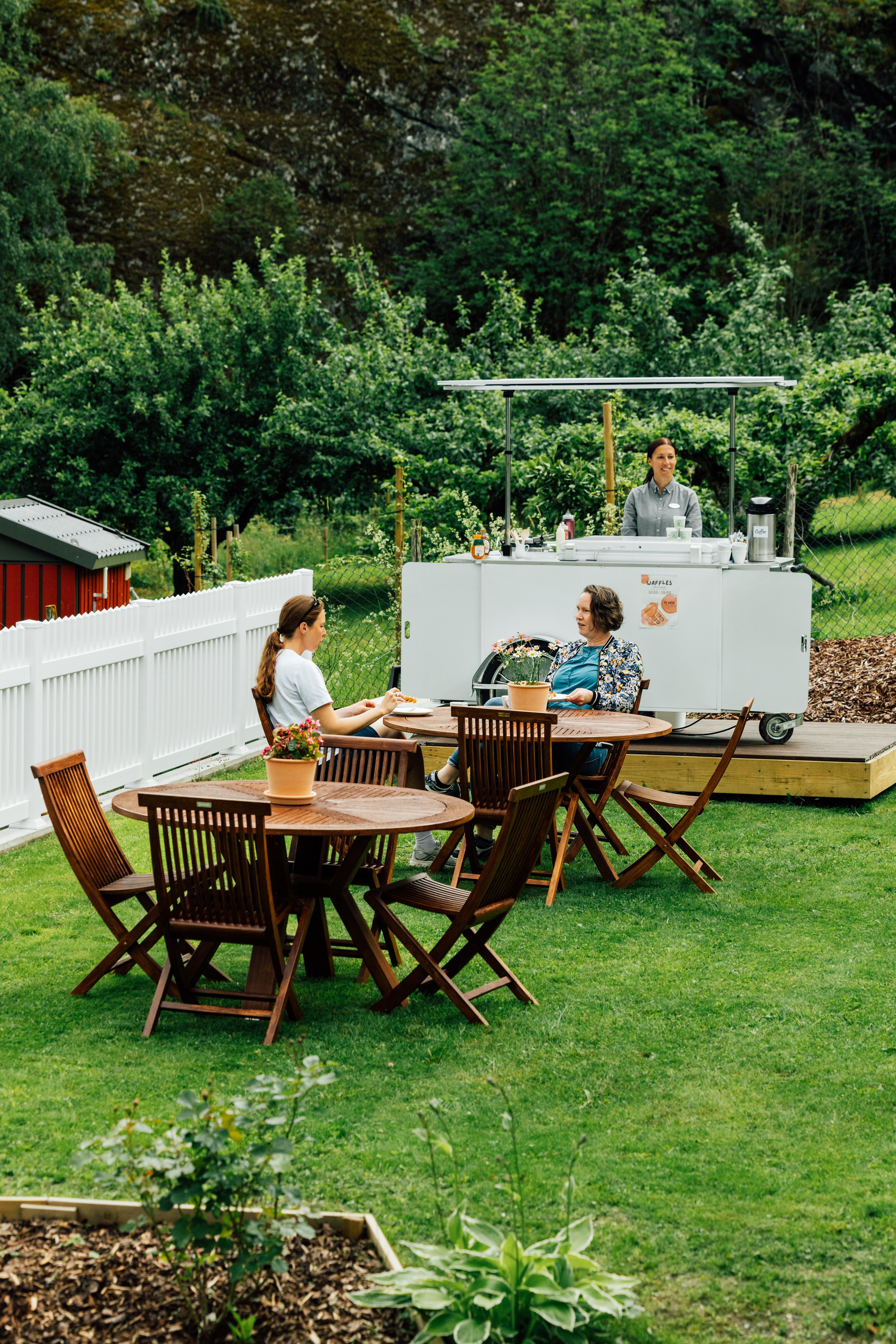 Two women sitting at a table in the garden, with the waffle cart in the background.