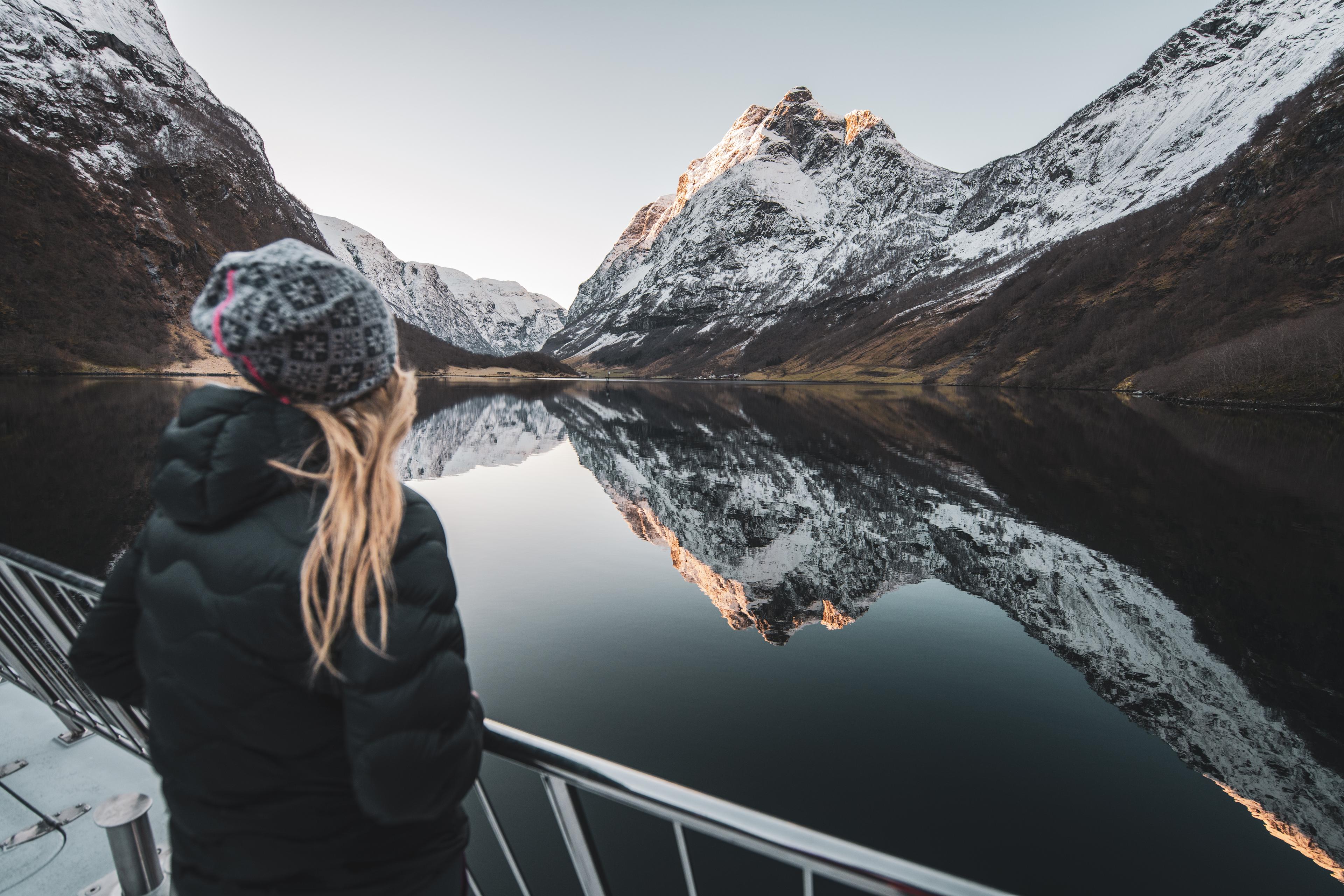 Girl on a fjord cruise admires a mirror-calm fjord and snow-covered mountains.