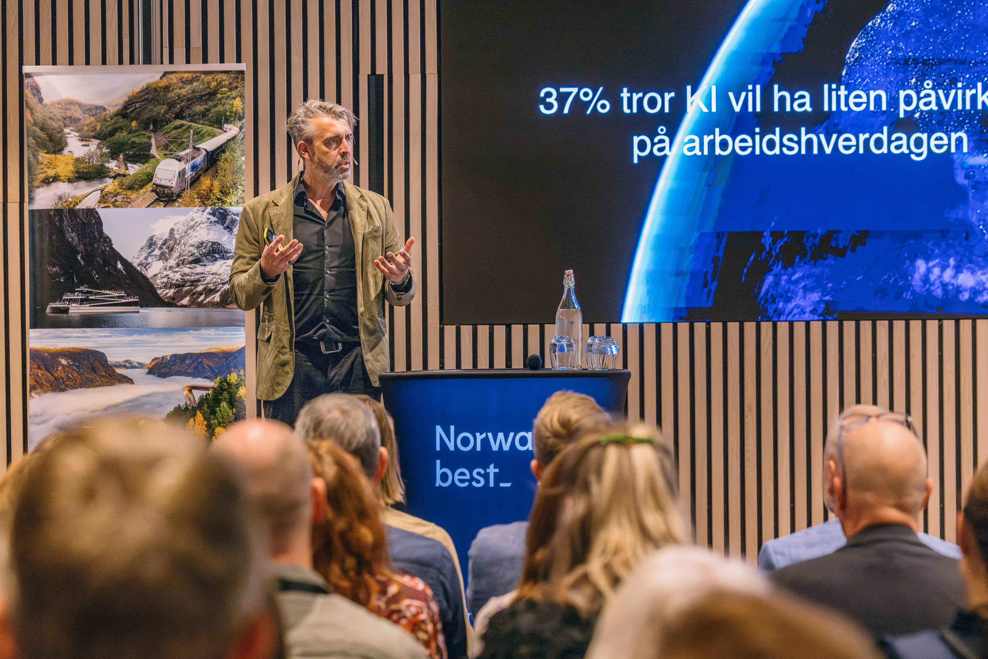 Foredragshaldar snakkar til publikum under konferanse, med presentasjon på skjerm i bakgrunnen.
