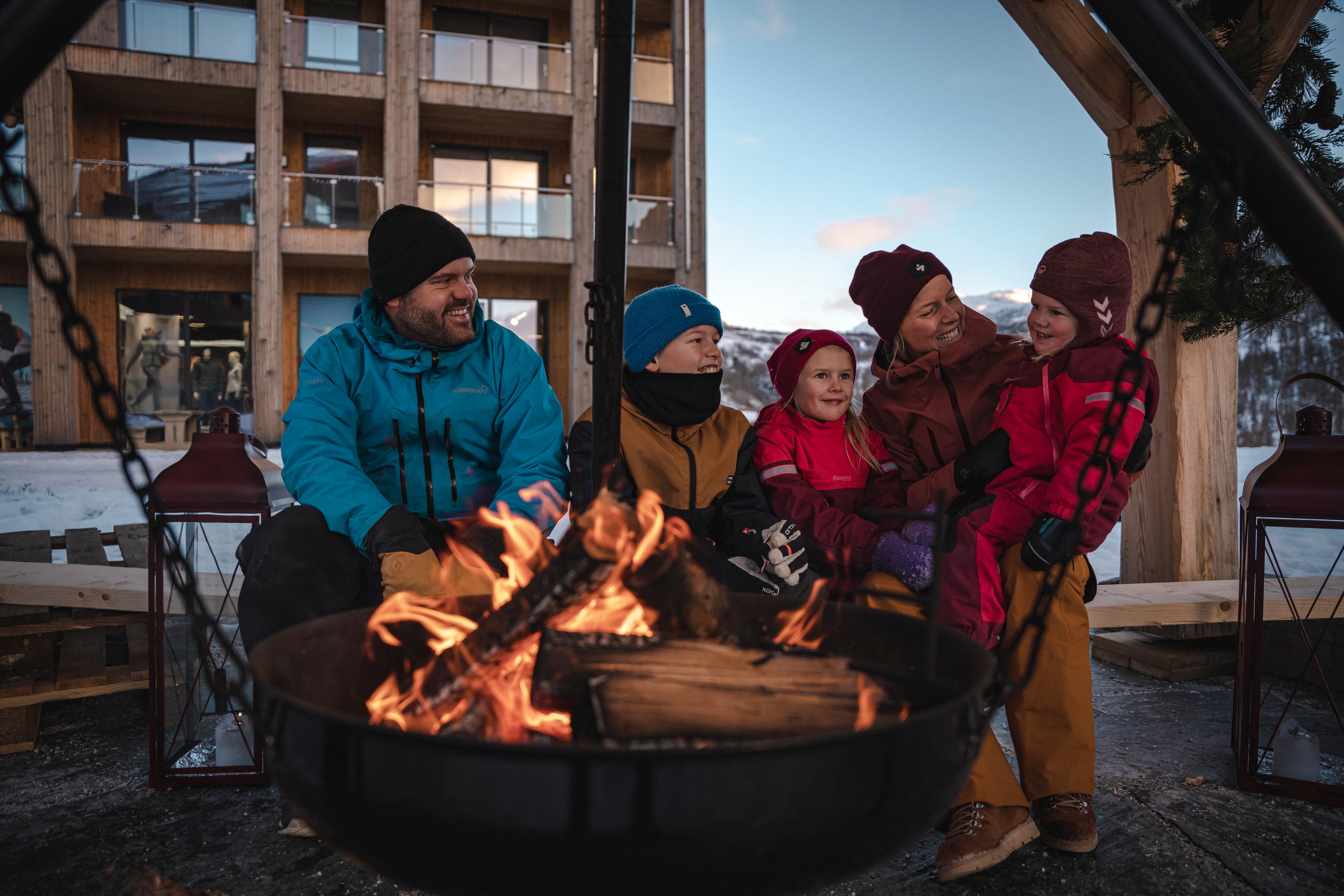 En familie koser seg rundt bålpanna foran hotellet en vinterdag.