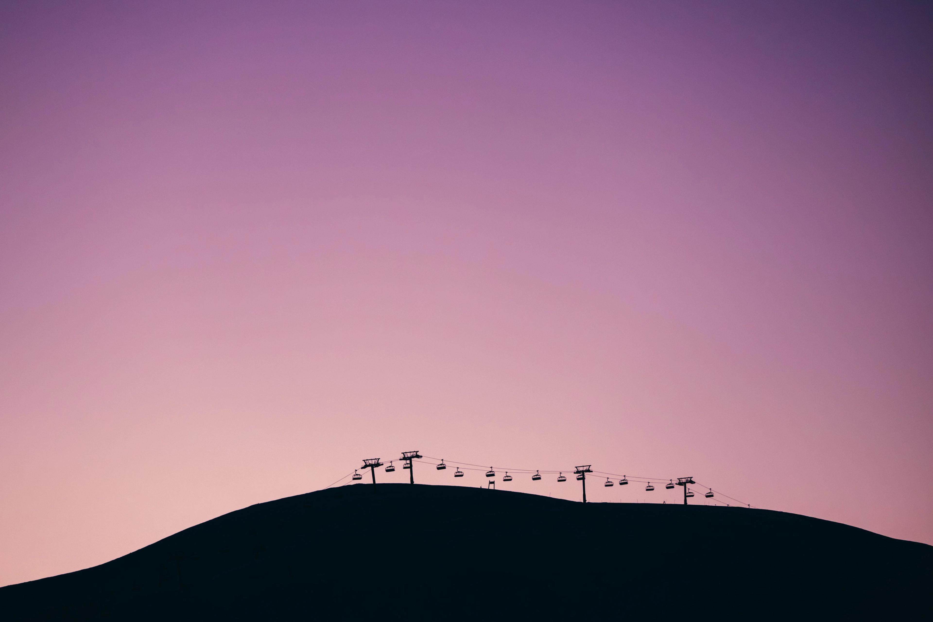 A ski lift on a mountain summit, silhouetted against a purple sunset.