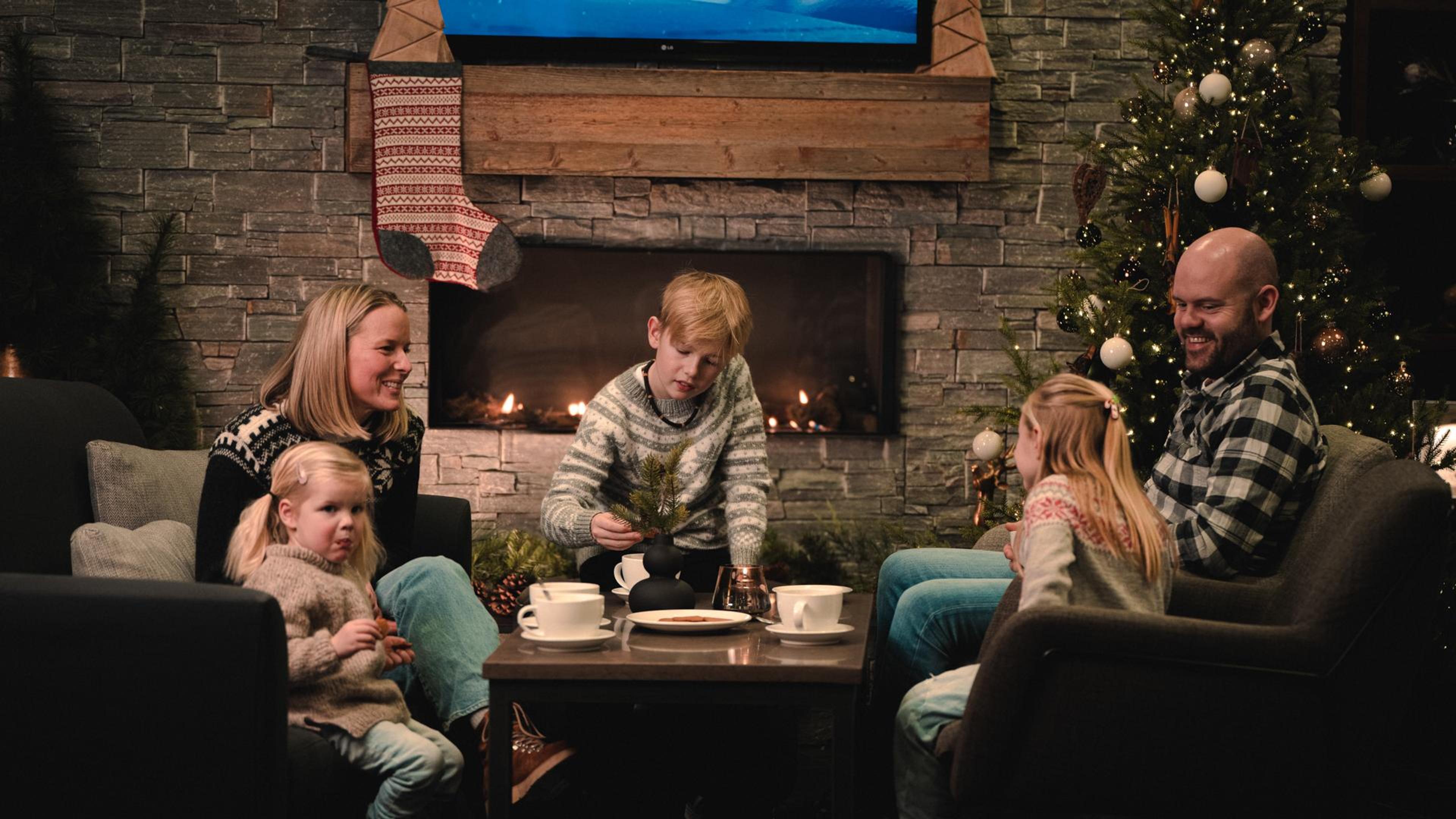 En familie koser seg foran peisen i en julepyntet stue med juletre.