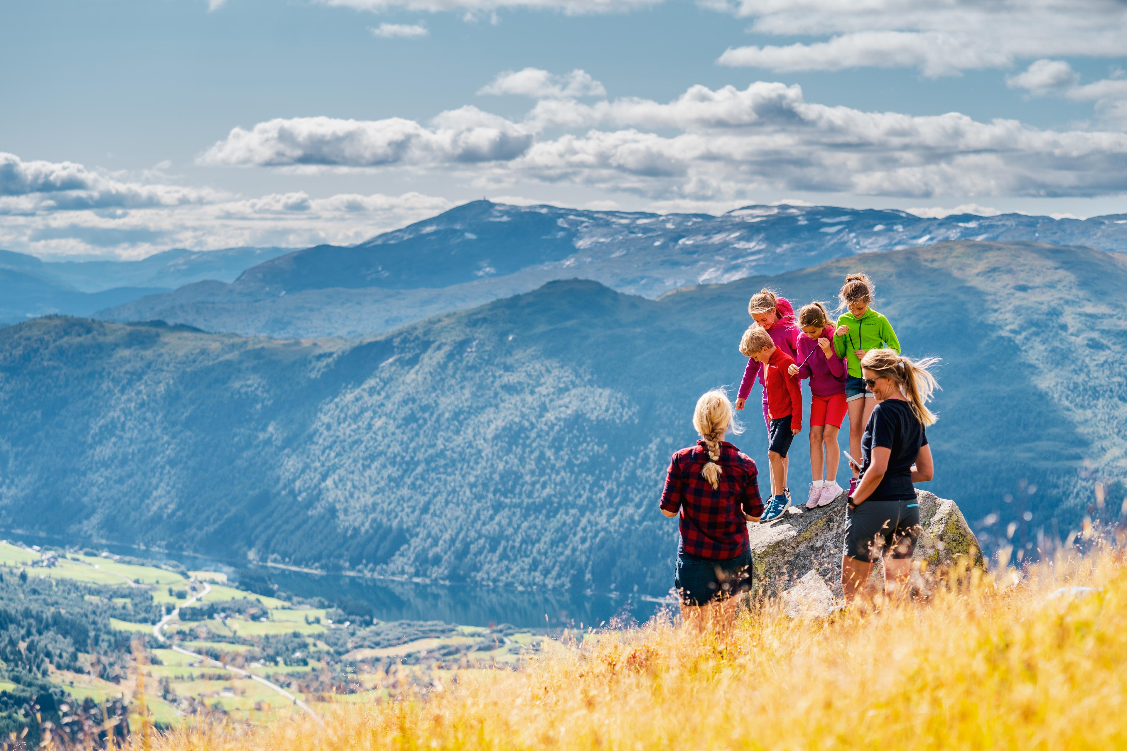 Familie på fjelltur ser utover dalen og fjellheimen en sommerdag.