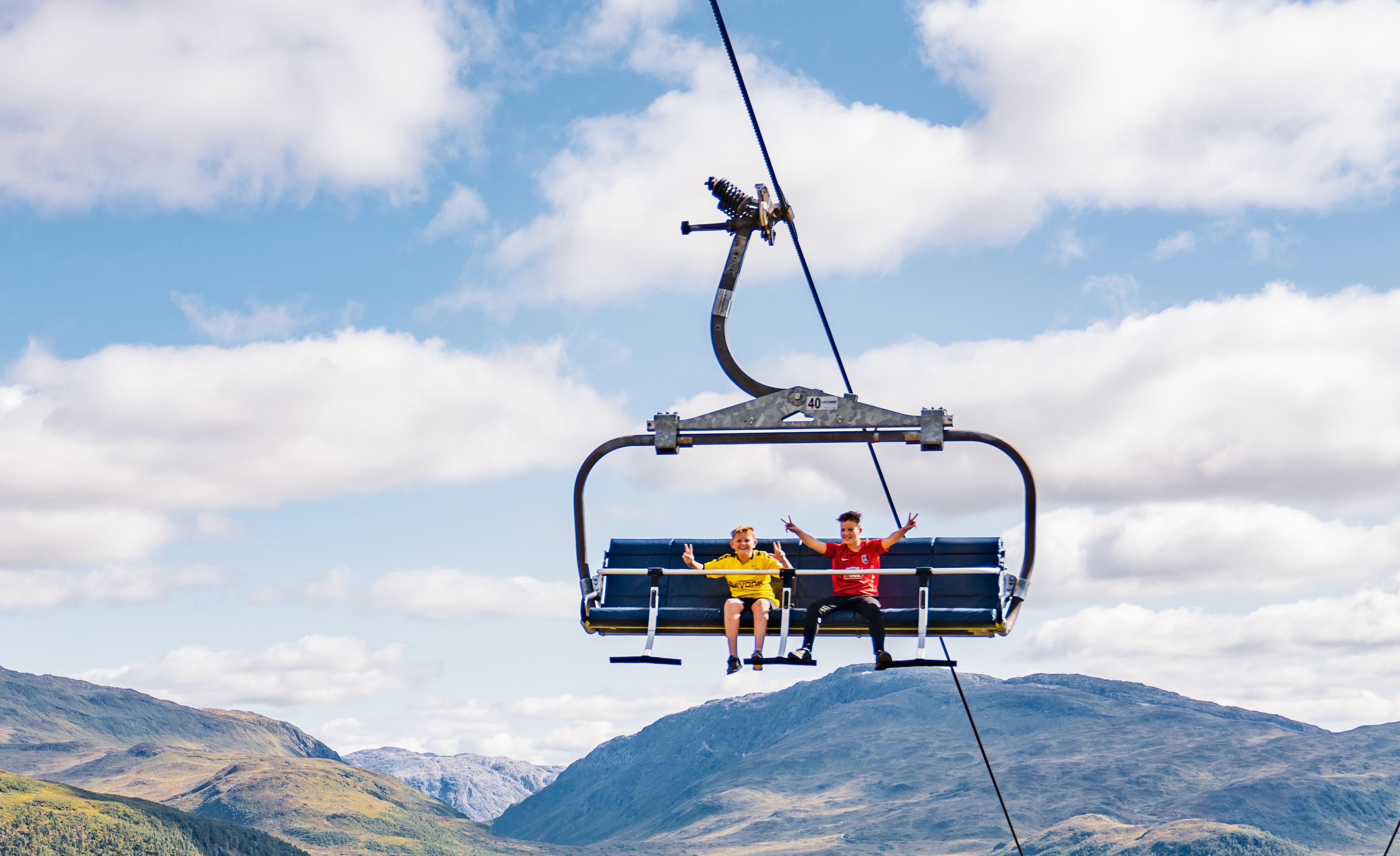 To gutter smiler og viser V-tegn til fotografen høyt oppe fra stolheisen.