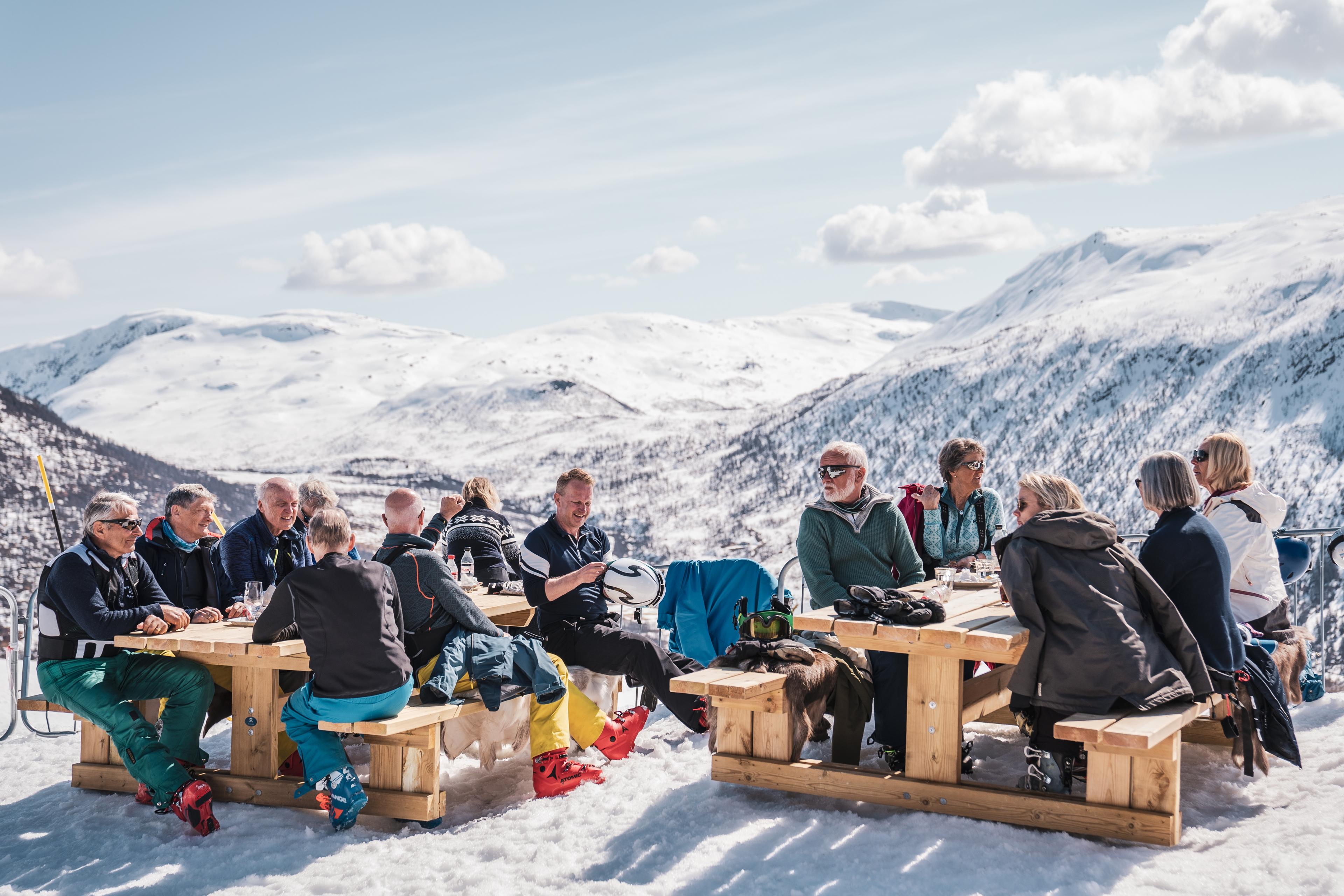 Skikjørere nyter en pause i sola på uteservering i bakken.
