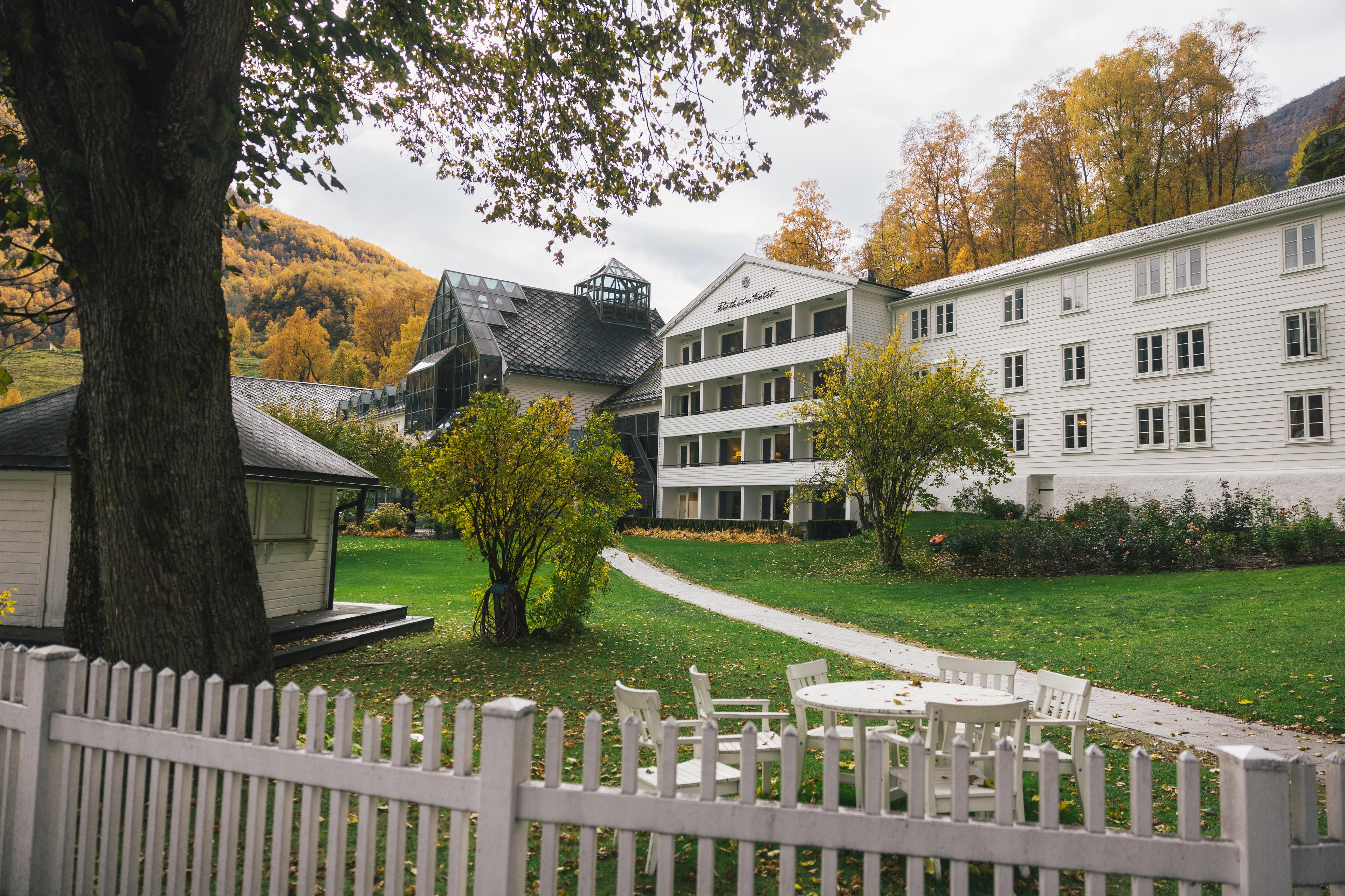 Fretheim Hotel sett frå hagen, omgitt av haustfarga tre og med kvite hagemøblar i framgrunnen.