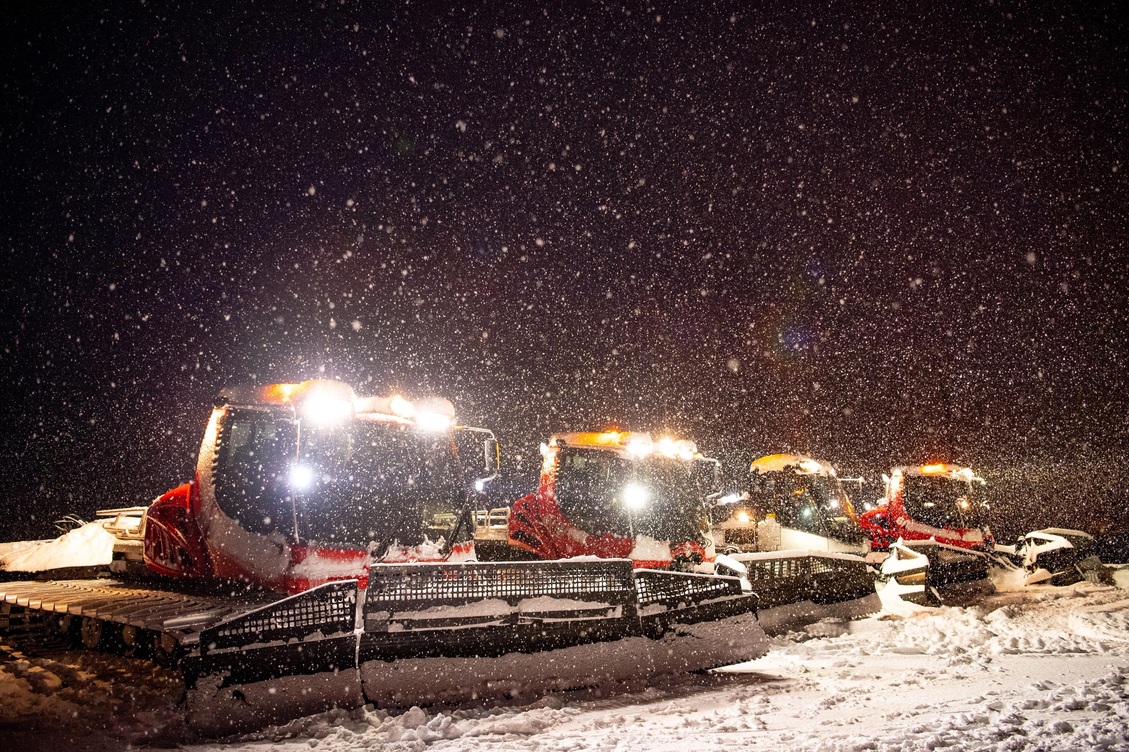 Four snow groomers in falling snow.