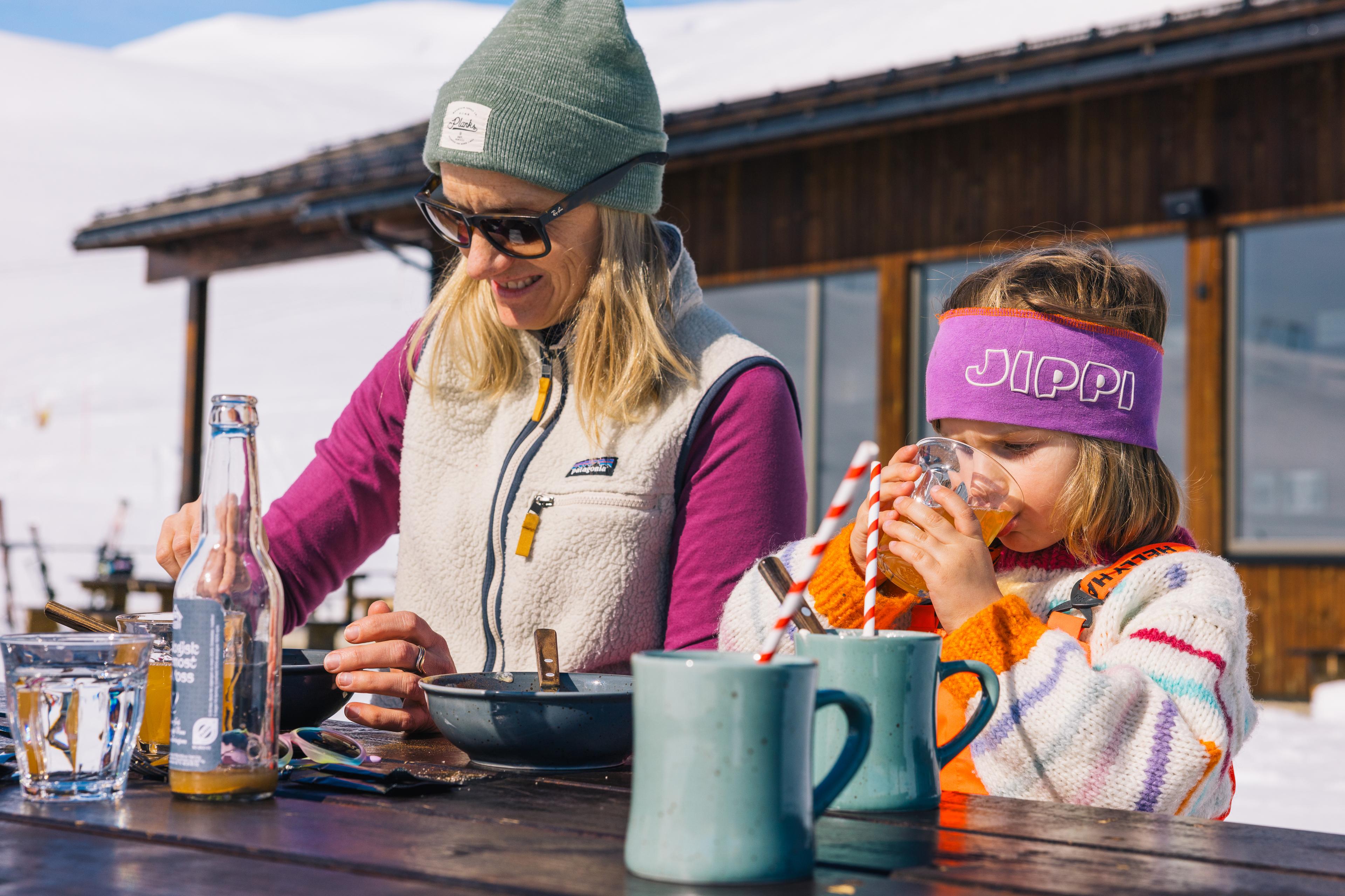 Mother and daughter take a lunch break in the sun on the outdoor terrace in the ski hill.