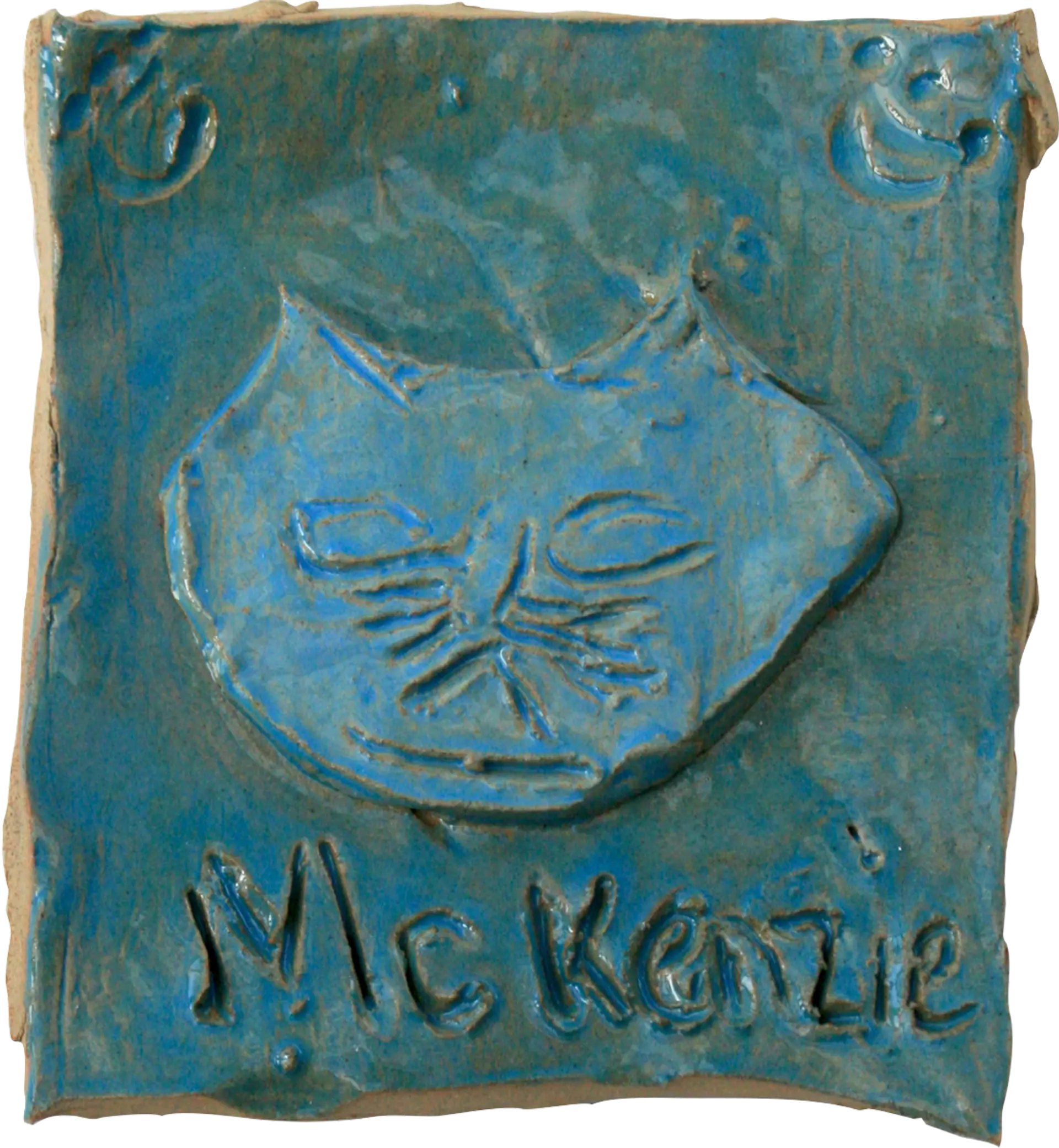 A blue glazed ceramic tile of Mckenzie, Lauren’s pet cat. His name is written at the bottom of the tile, and paw prints decorate the top corners. 