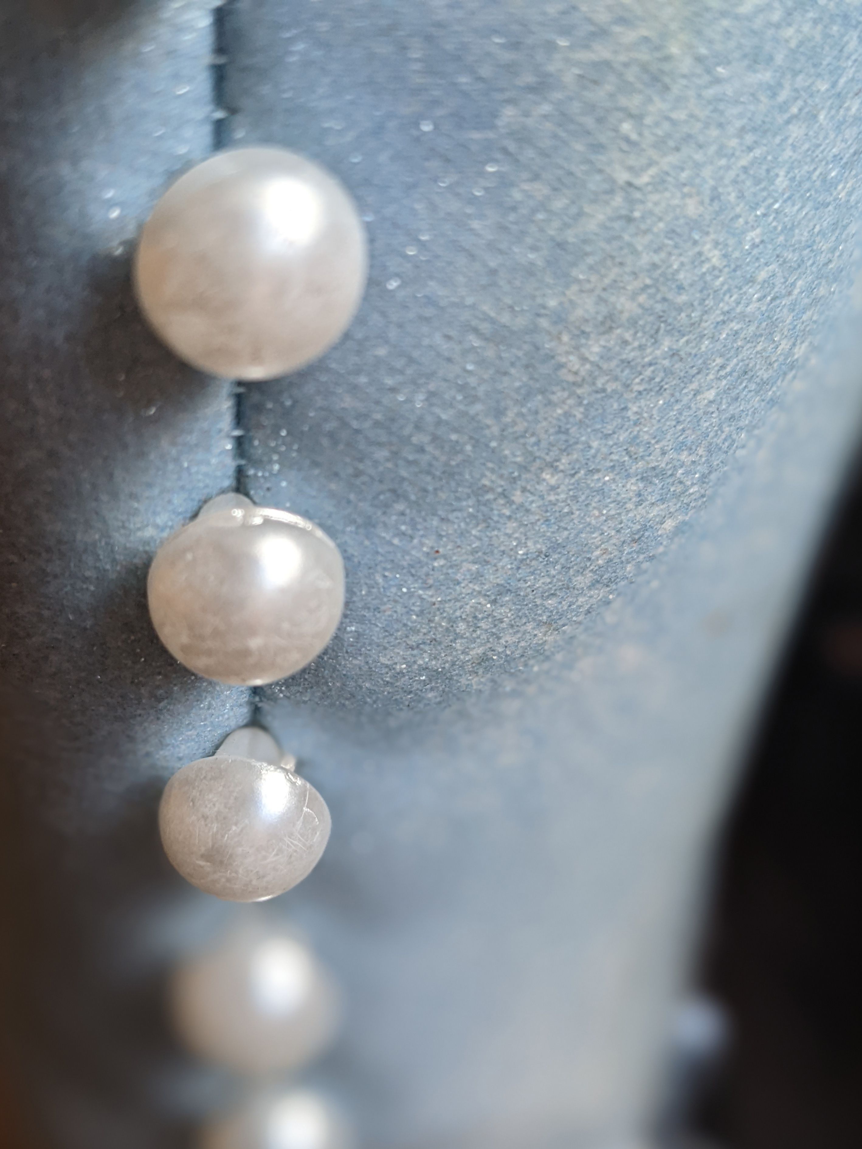  An abstract photo of light blue material with pearl adornments, unfocused at the bottom of the picture. It is not clear what the item is.