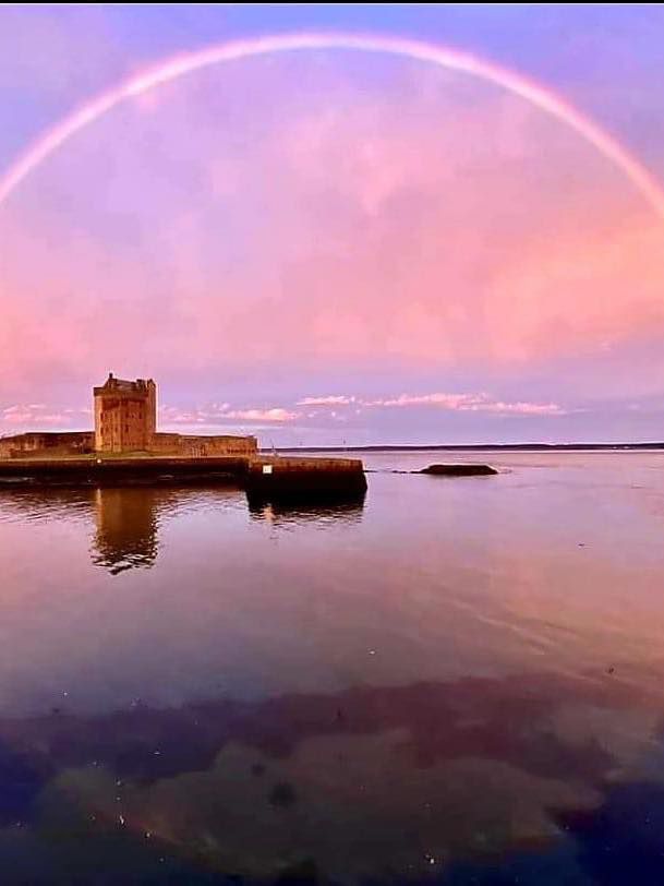 A luminescent pink and purple sky with a silver tinted rainbow arching into a full semi-circle over water, the rainbow’s reflection makes a complete circle. It is Broughty Ferry, the castle and harbour wall are also in the picture. In the bottom left corner, in white text it reads, ‘Amanda 28/06/2021.