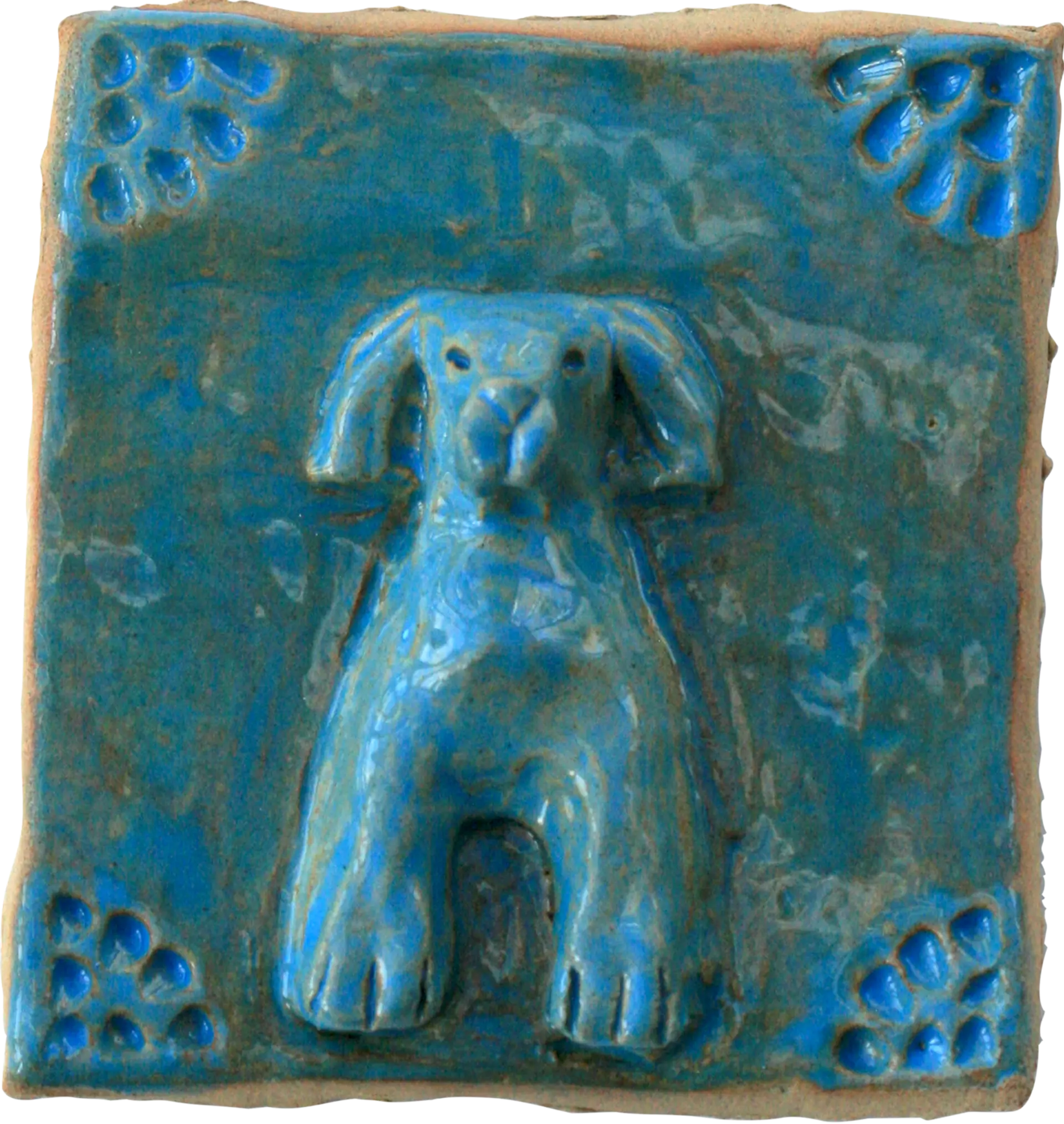 A blue glazed ceramic tile of Alexander’s dog Miggins. The corners of the tile are decorated with petal shaped indents. 