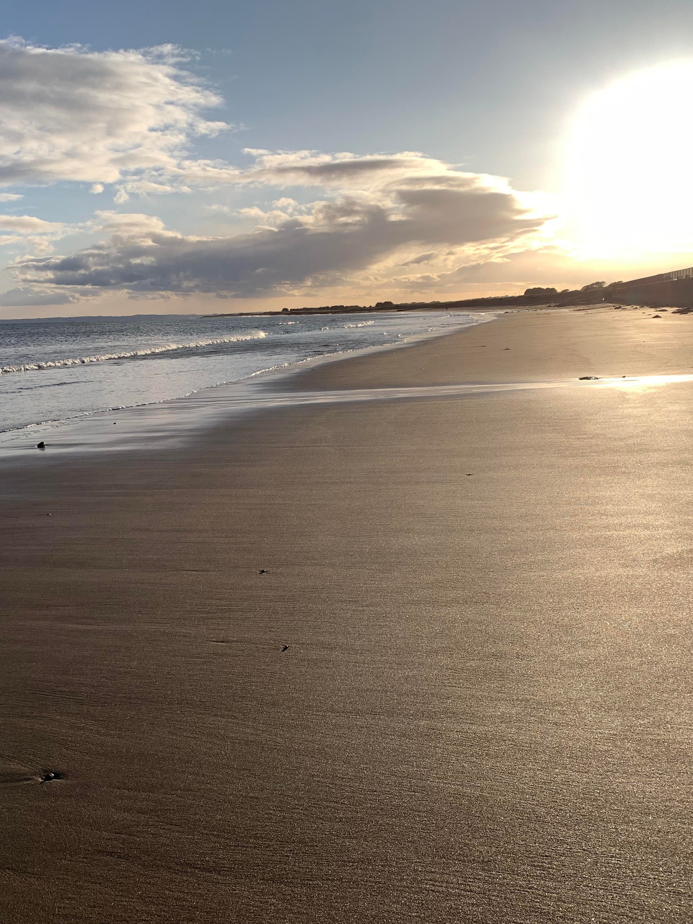 A long flat of sand and sea with a blindingly bright sky, looks like a winter sun.