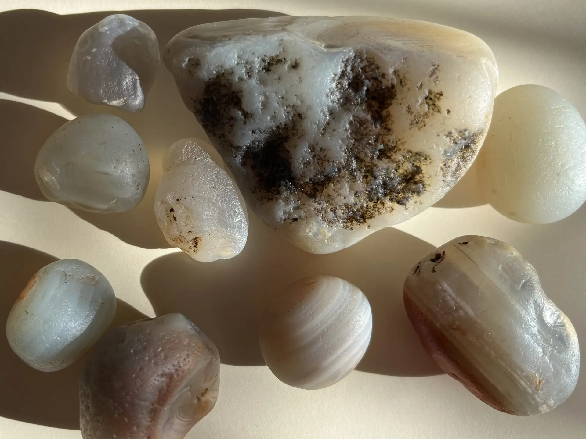 A collection of nine agate stones. They vary in size and pattern and are displayed in sunlight, casting shadows across the image.
