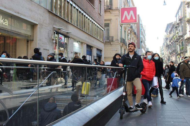 A man with an Augment e-scooter in a crowd in front of metro station