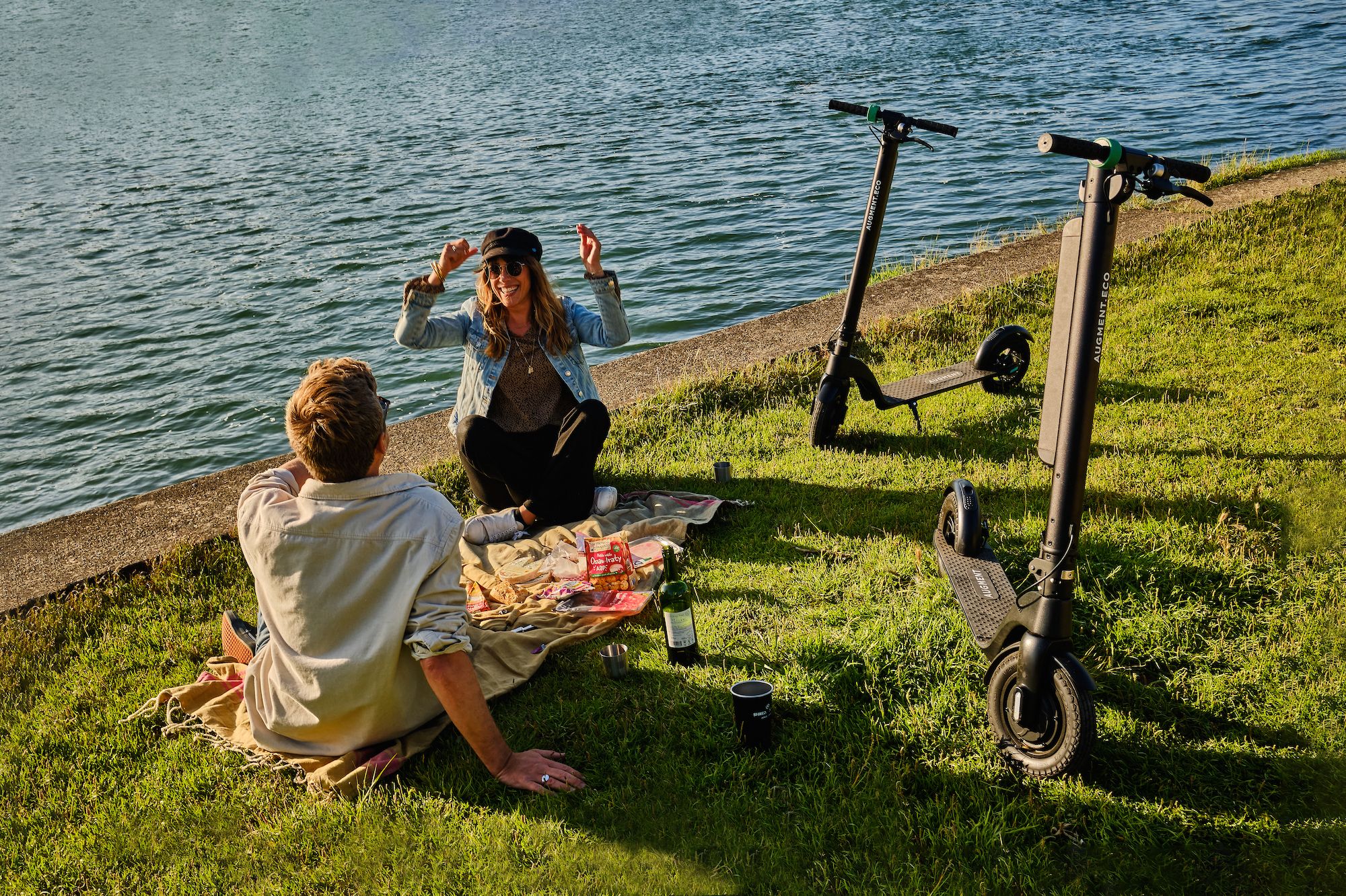 A man and a woman on a piknik with two Augment e-scooters next to them