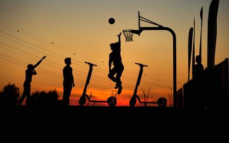 Monopattini in secondo piano con persone che giocano a basket in primo