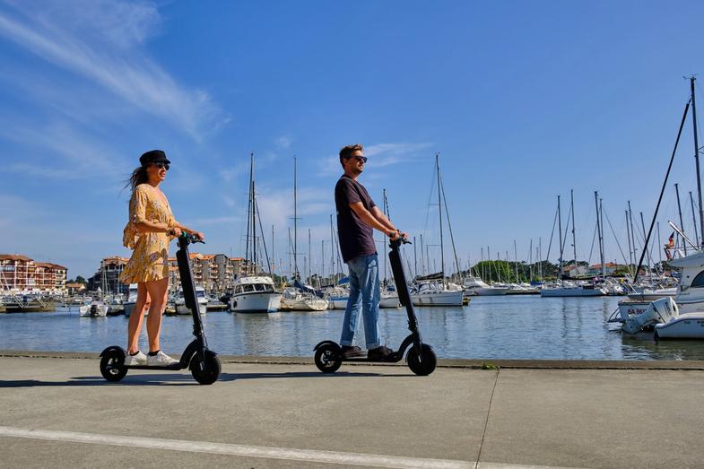 Une femme et un homme conduisent un scooter électrique Augment à côté du port de la ville.