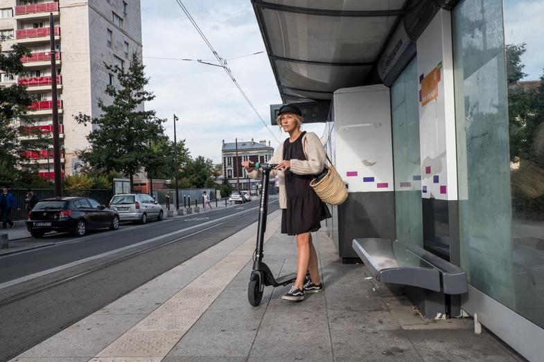 Une femme attend le tramway avec sa trottinette