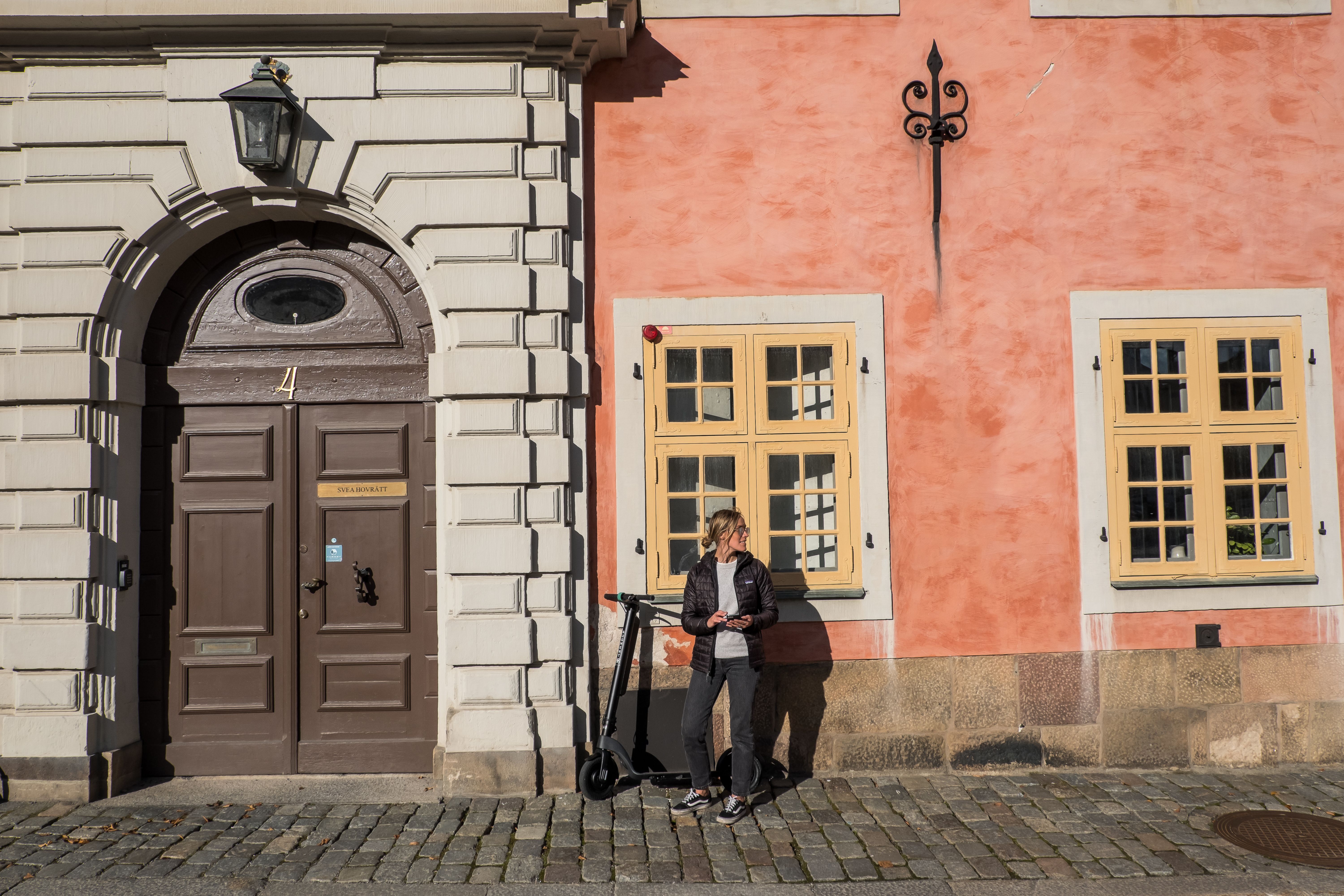En kvinna med en Augment-elrullator står framför en gammal byggnad i en stad.