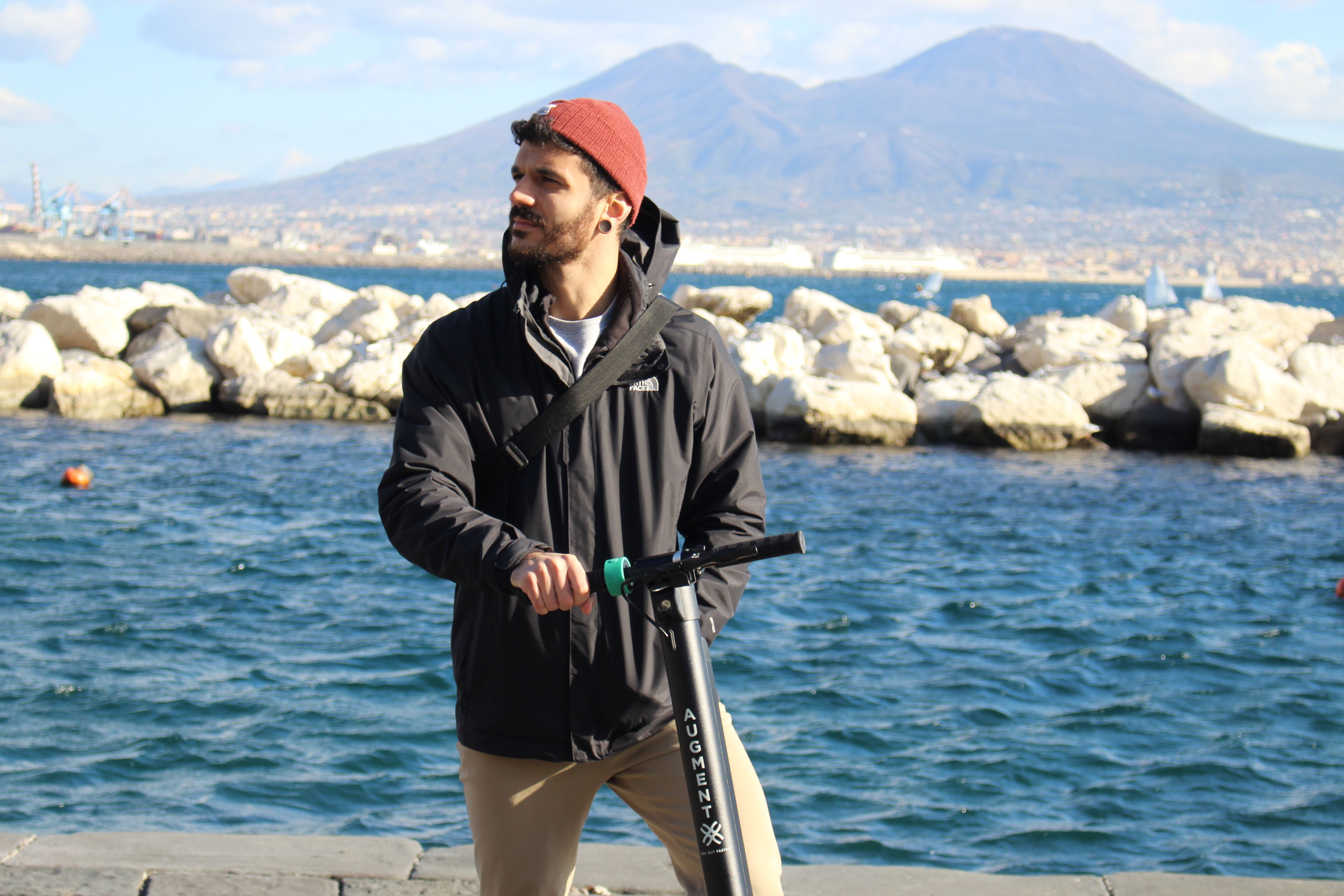 Un uomo in piedi con un e-scooter Augment sulla strada vicino al mare