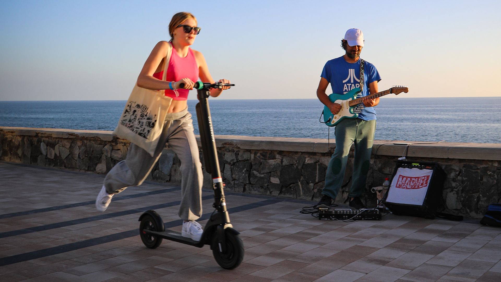 Una donna in sella a un e-scooter Augment passa davanti a un artista di strada sul lungomare