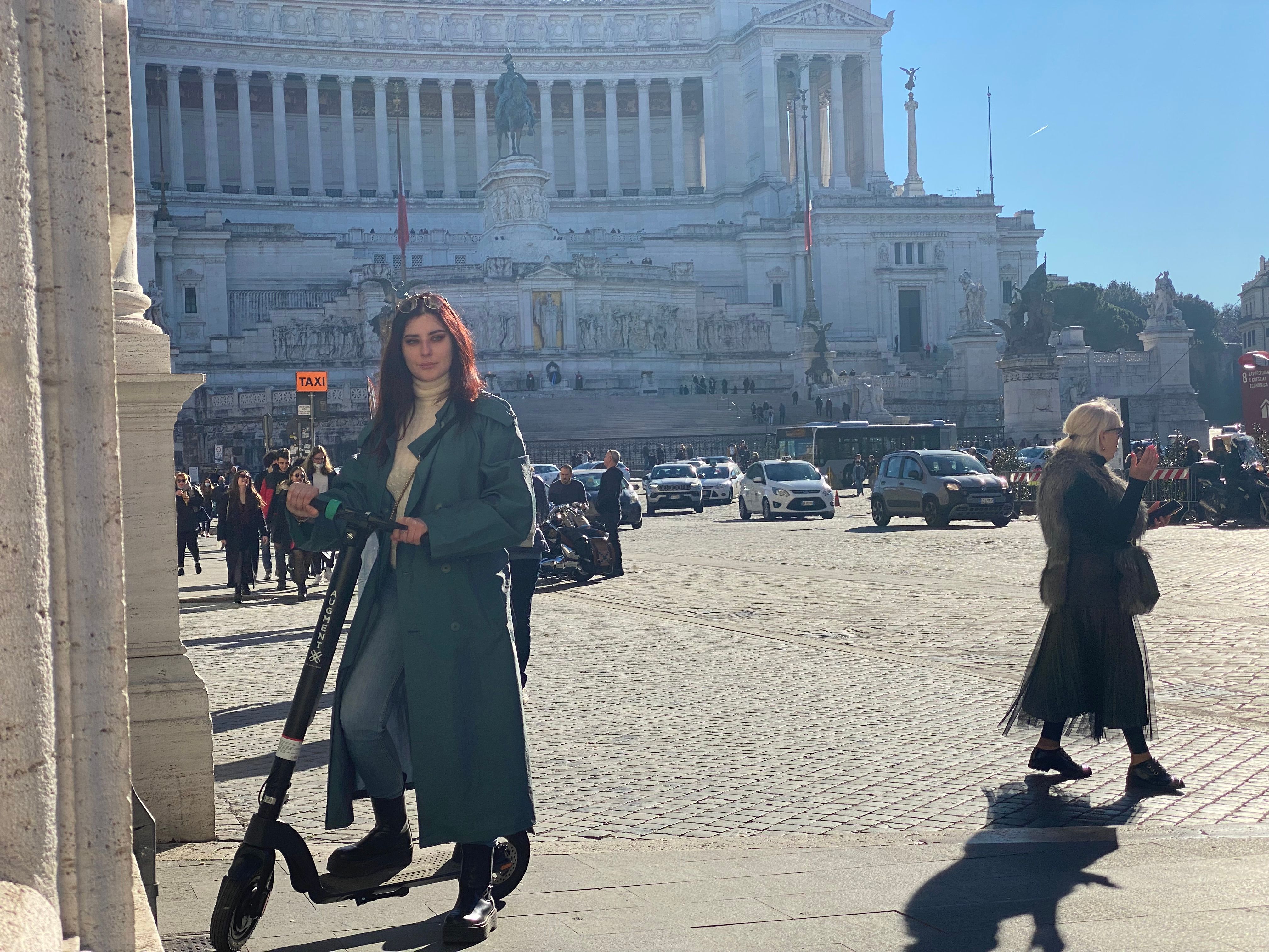 Una donna in piedi con un e-scooter Augment nella piazza della città