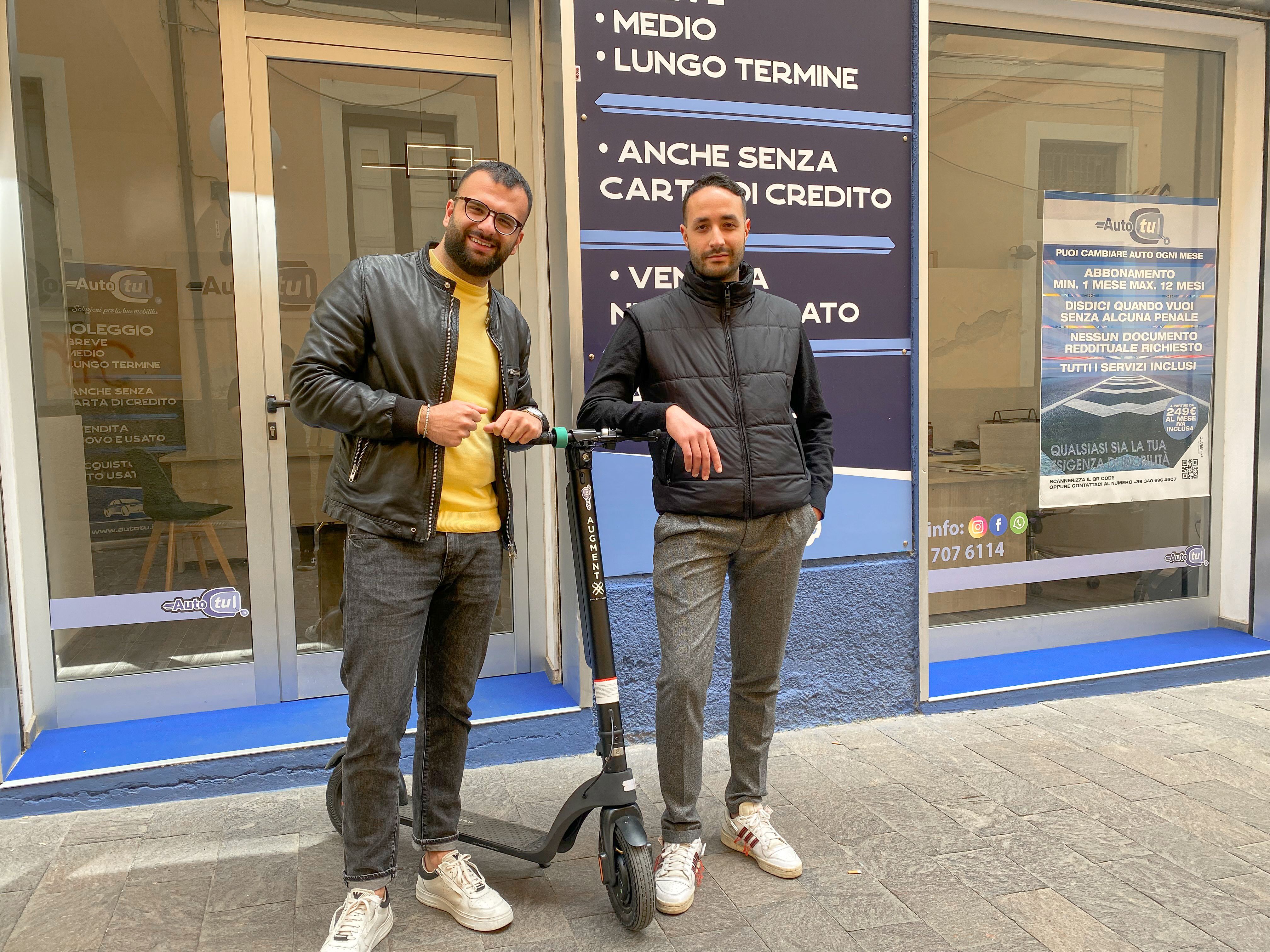 Due uomini in posa con un e-scooter Augment davanti a una boutique