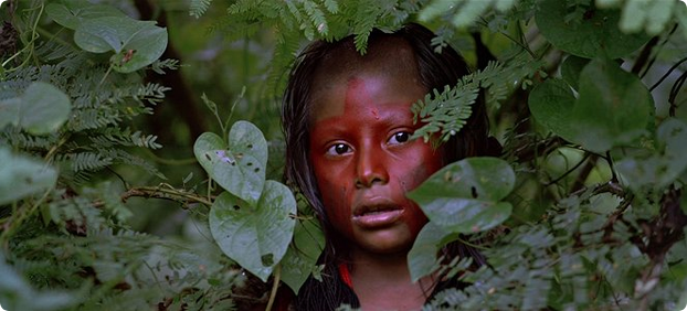 Et bilde fra filmen Baraka fra 1992, en liten afrikansk gutt titter frem mellom løvverket i en jungel